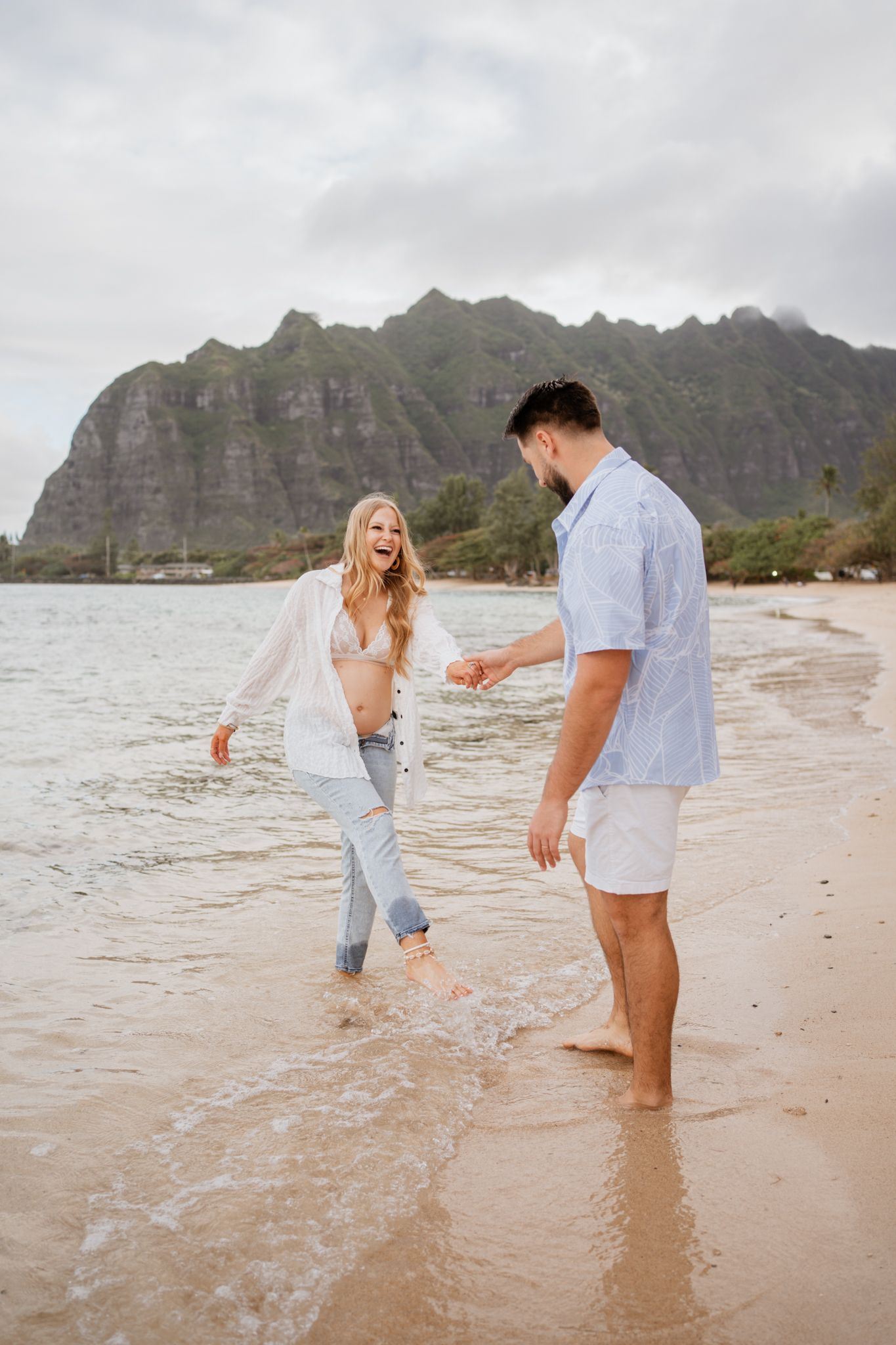 Couple playing and splashing in ocean waves with dramatic mountain backdrop.
