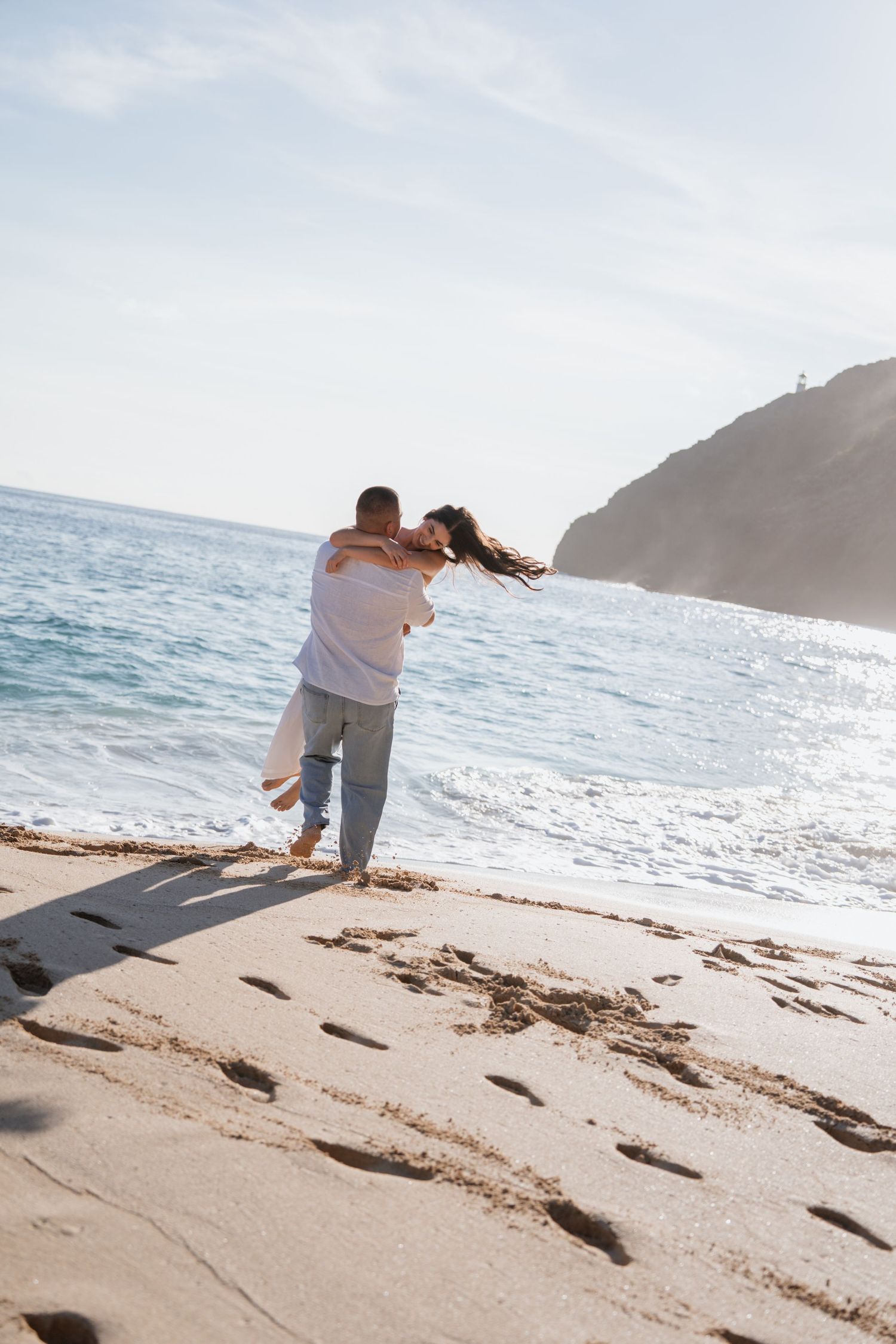 Romantic couple shares tender moments on a sunny beach with waves and cliffs in the background. Oahu photoshoot, Honolulu, Waikiki