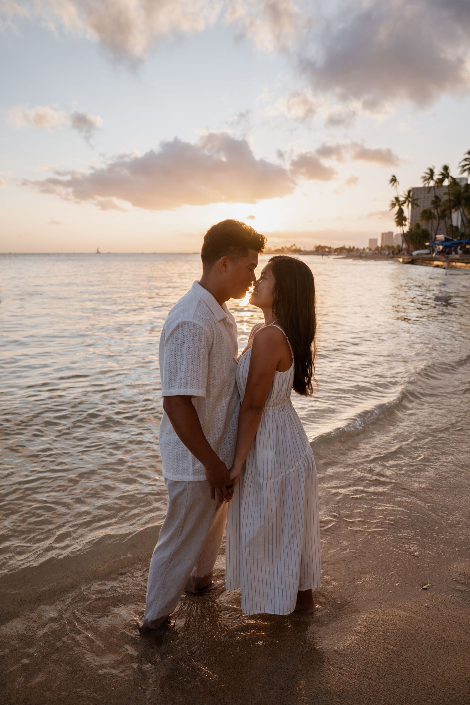 A couple shares a romantic moment at sunset on a tropical beach shoreline.