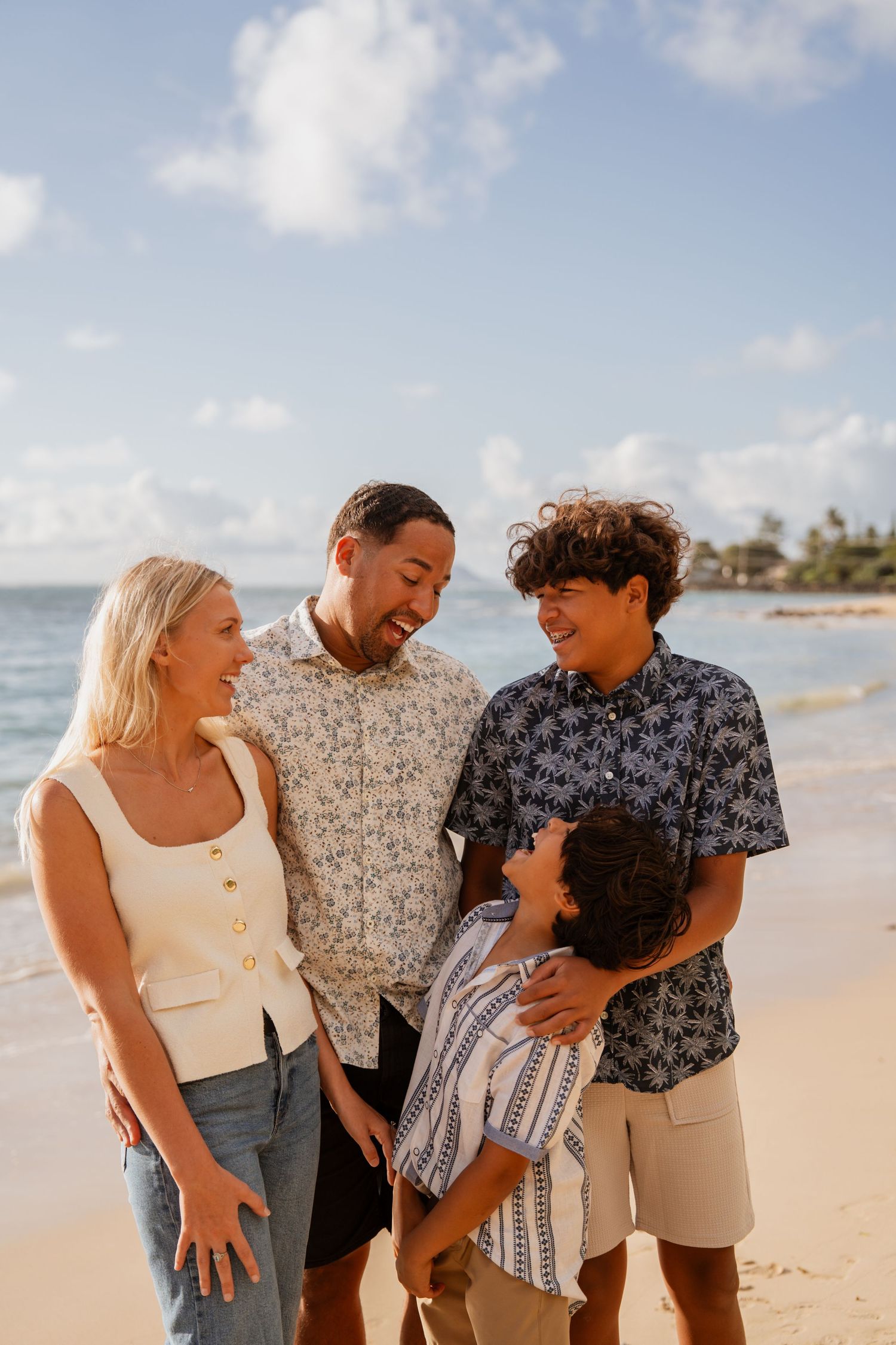 A family of four enjoying a sunny day together on a tropical beach with palm trees in the background.
