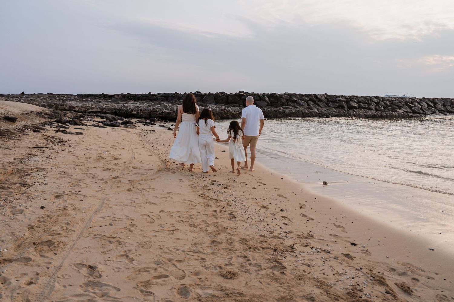 Family walking together on beach holding hands at sunset.