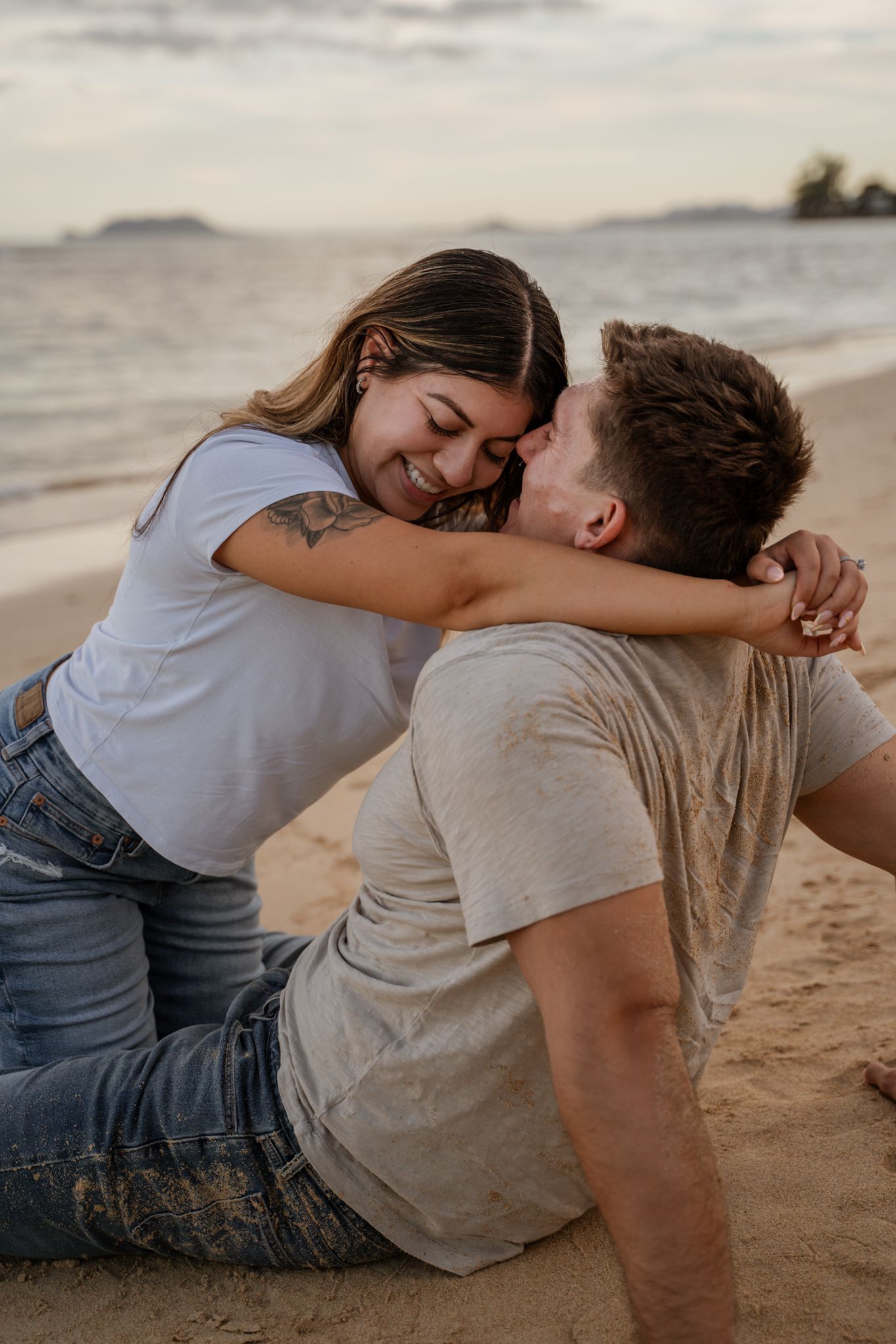 A couple shares an intimate moment while sitting on a sandy beach at sunset.