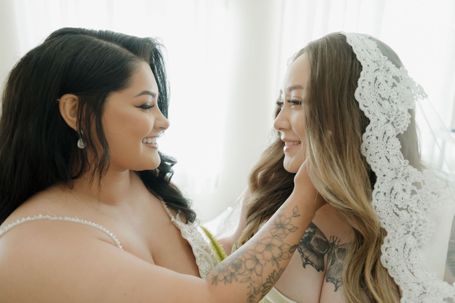Two people in lace and white getting ready for a wedding celebration in natural light.