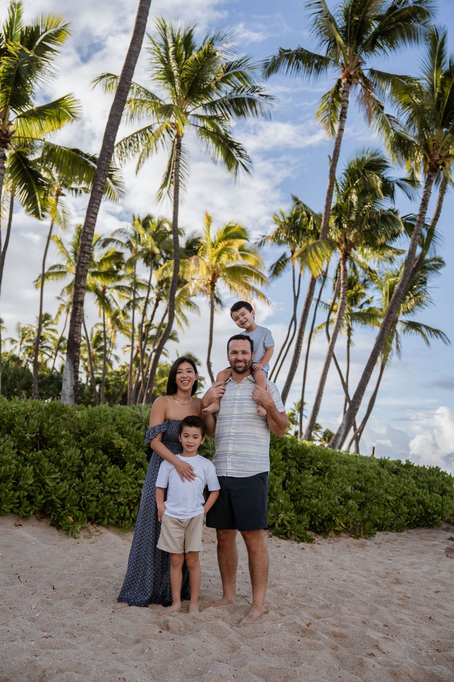 A family enjoys a tropical beach vacation with palm trees swaying in the background on a sunny day. Ko Olina Photographer