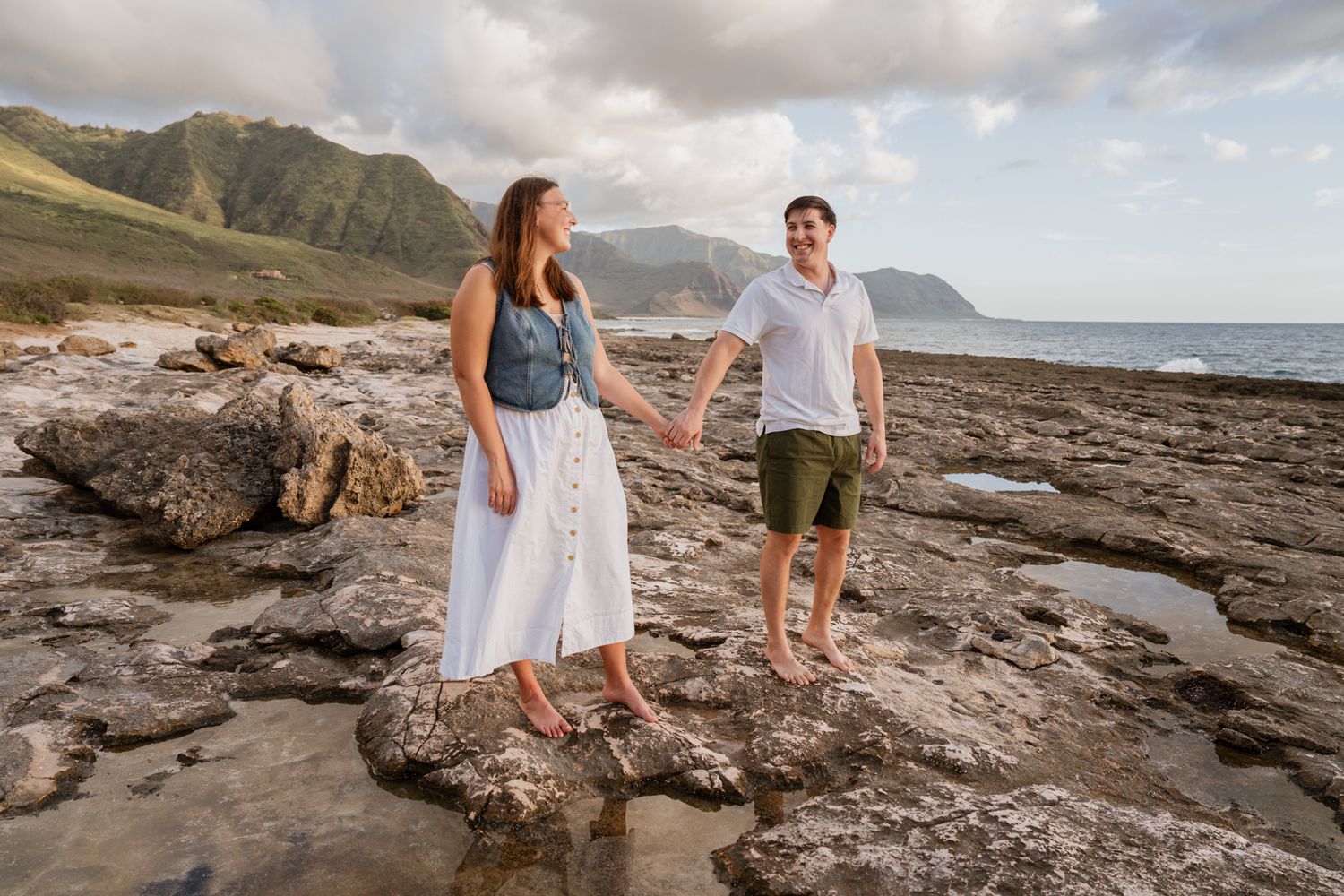 Couple exploring rocky coastline with dramatic mountain range in background.