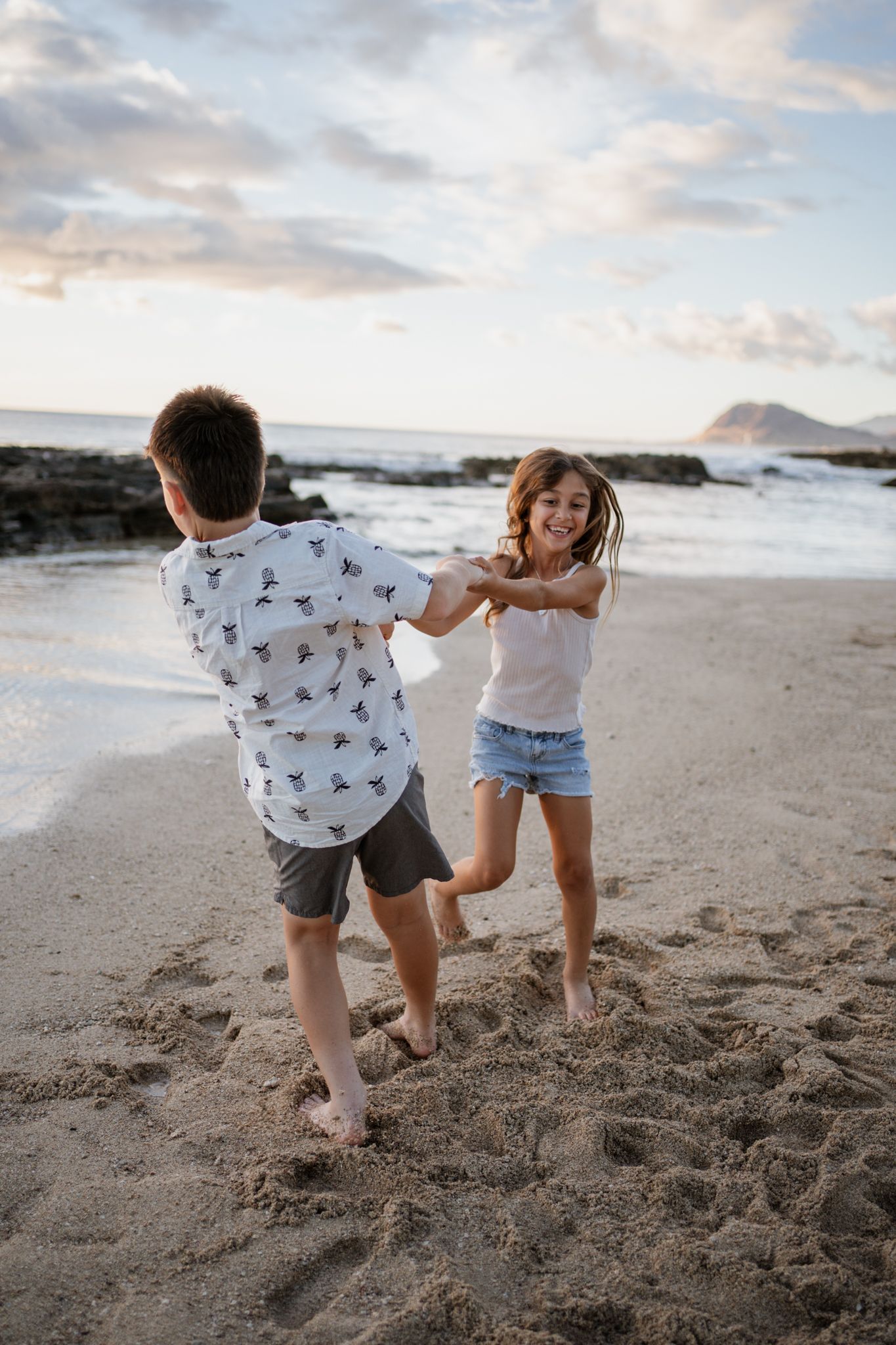 Two people dancing and playing together on a sandy beach at sunset.