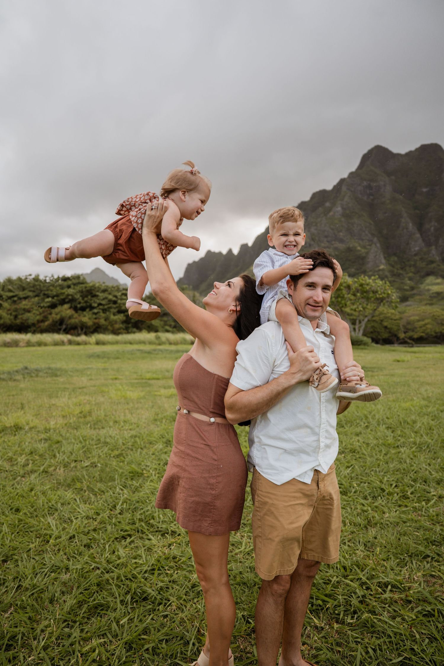 A couple shares a playful moment together in a lush green field with dramatic mountain scenery in Hawaii.