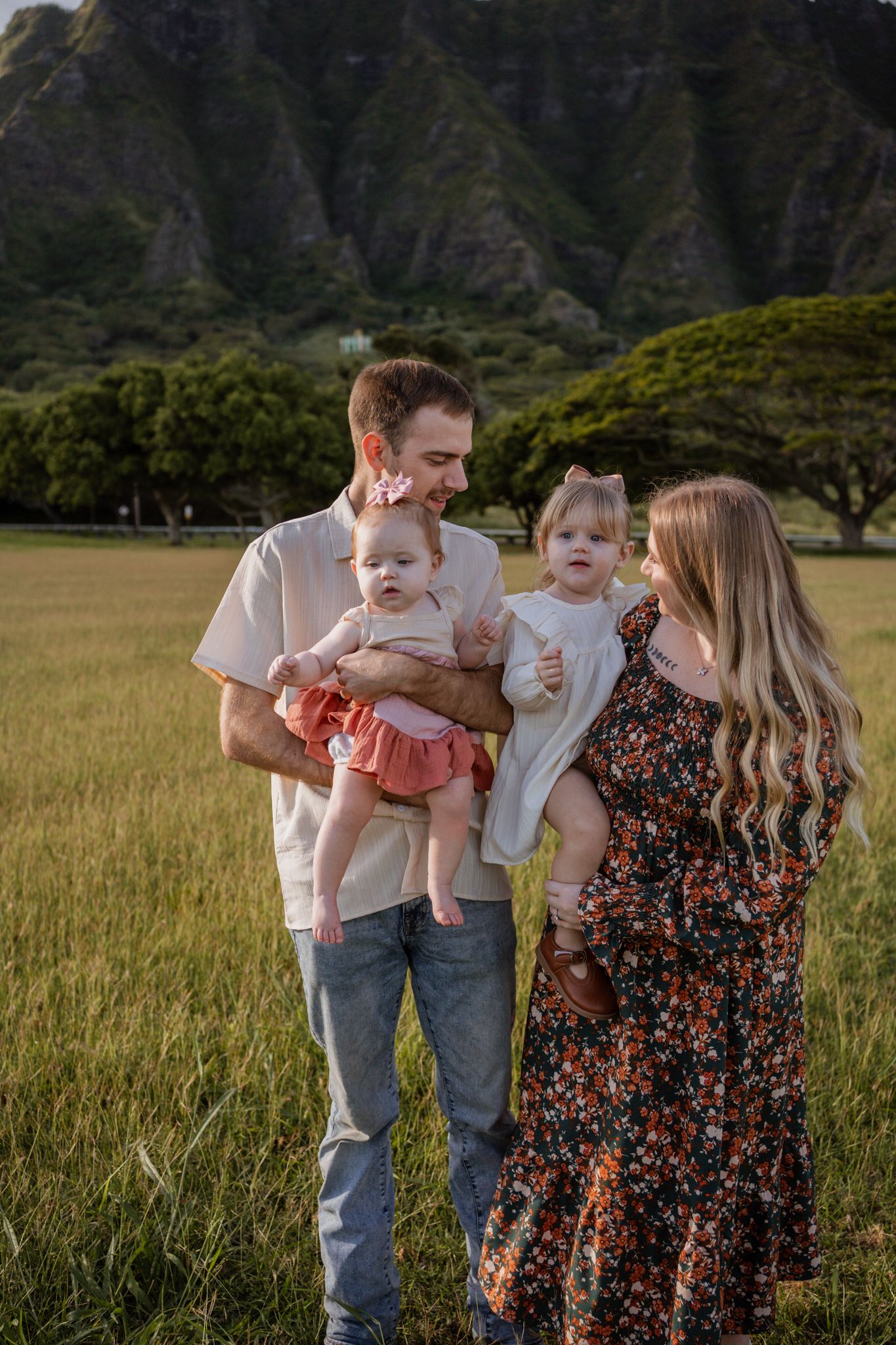 Family with small children posing in field with mountain backdrop in Hawaii.