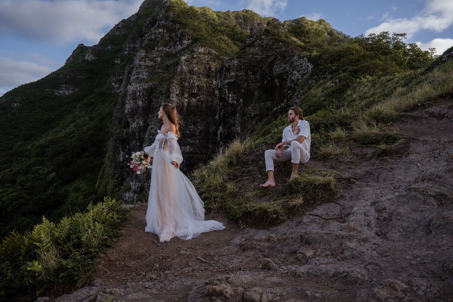 Romantic proposal scene on mountain trail with dramatic cliffs and cloudy sky backdrop.