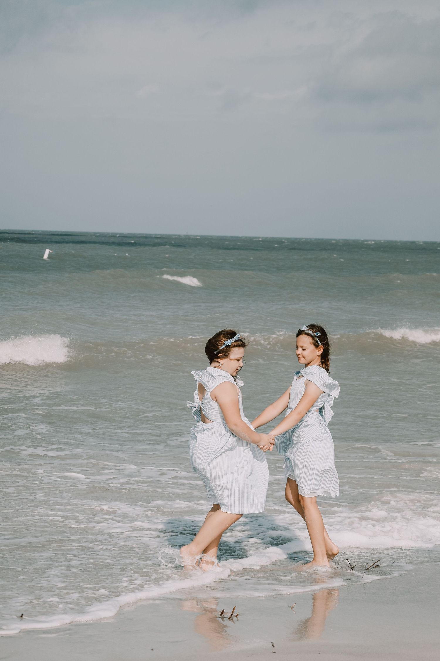 Two people in white dresses dance together in the ocean waves at the beach.