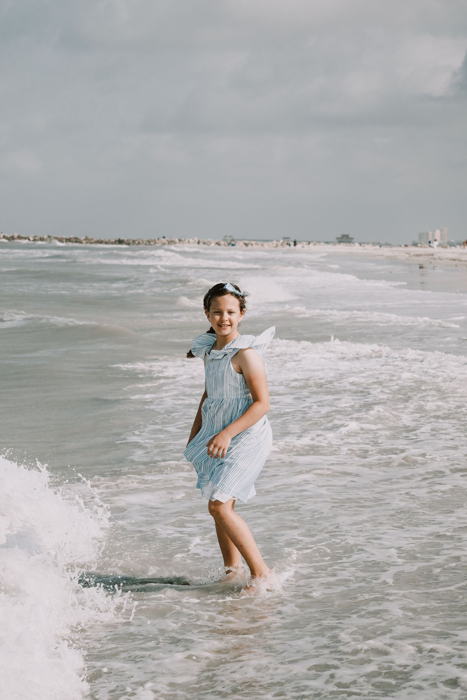 Child jumping through ocean waves in light blue dress at the beach.