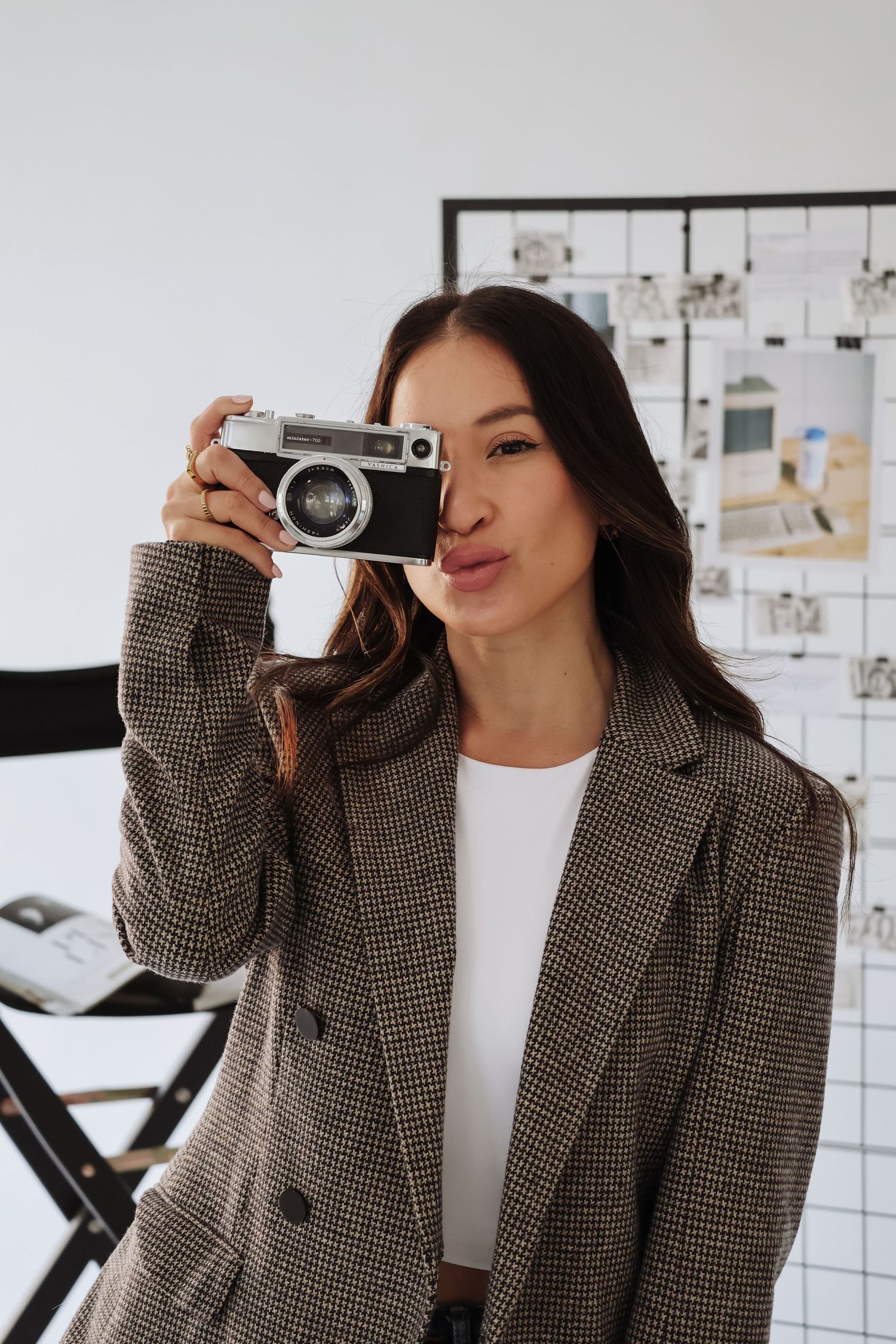 Stylish portrait with vintage camera and plaid blazer against white background.