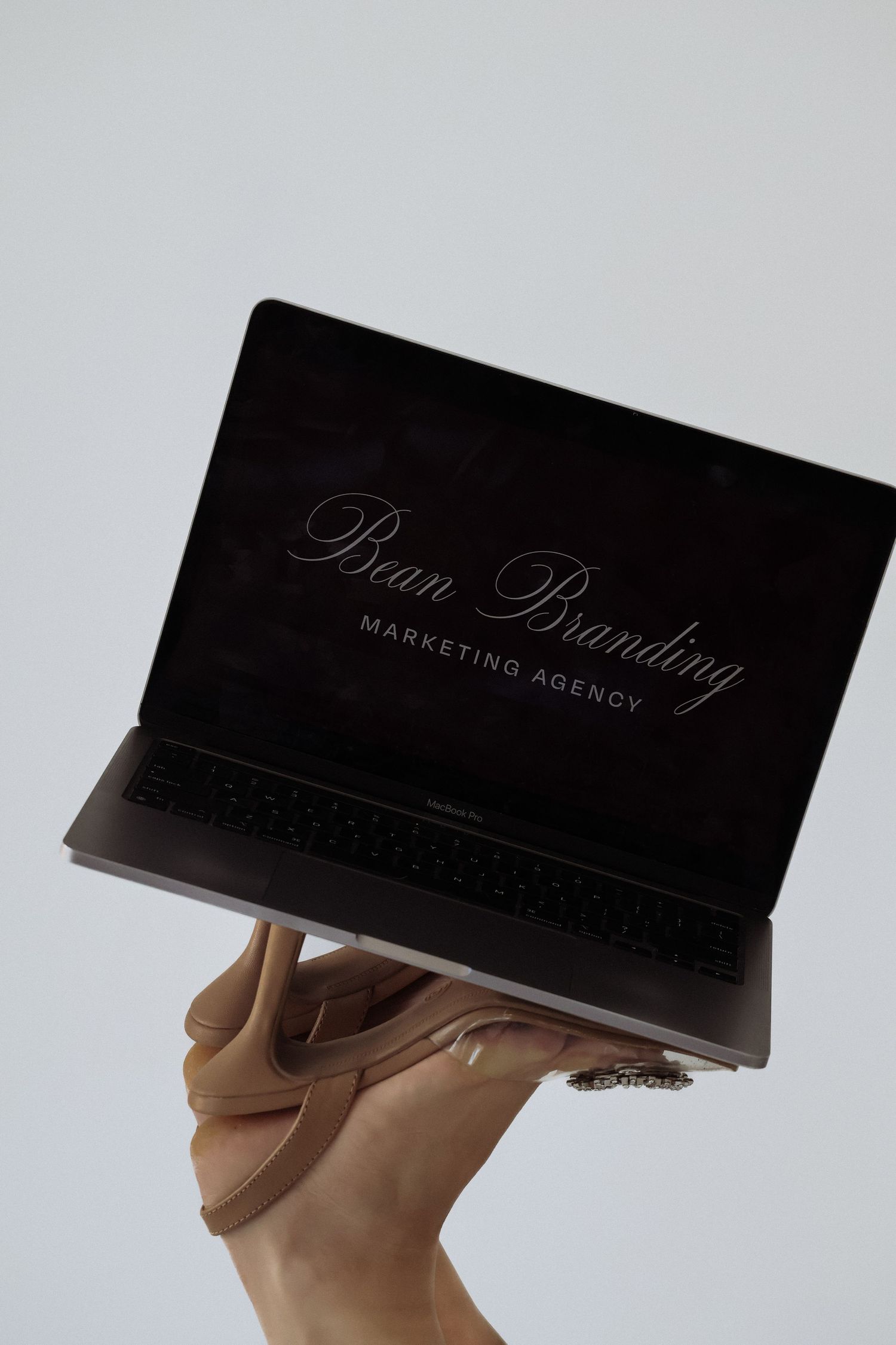 Hand holding laptop displaying Pure Branding Marketing Agency logo on dark screen.