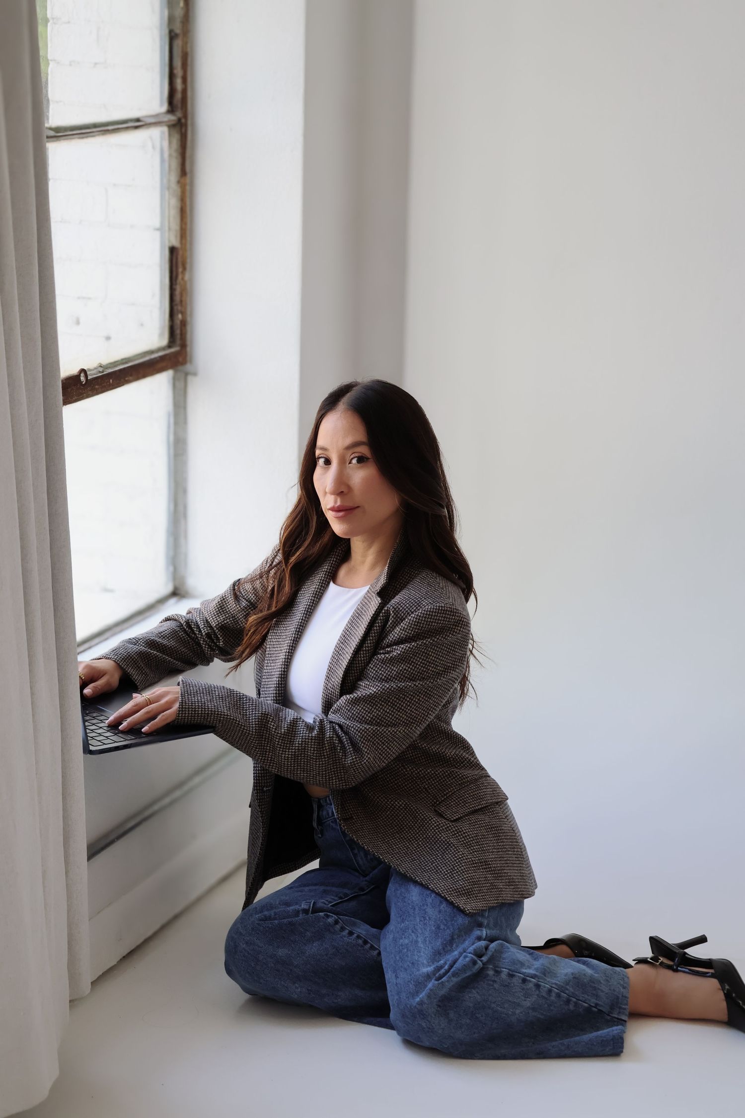 Professional seated by window in business casual attire working on laptop.