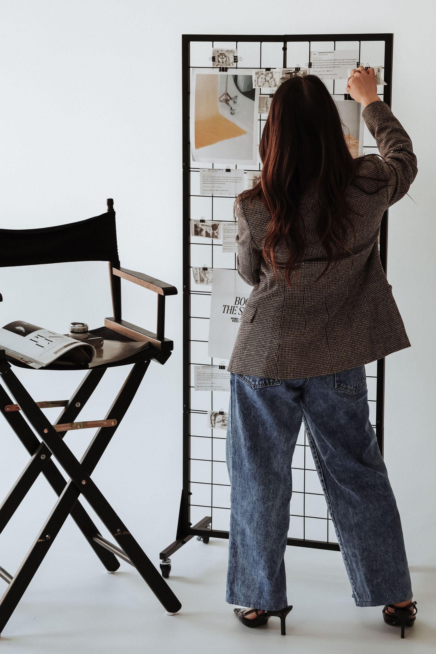 Person in blazer arranging items on wire grid board next to director's chair.