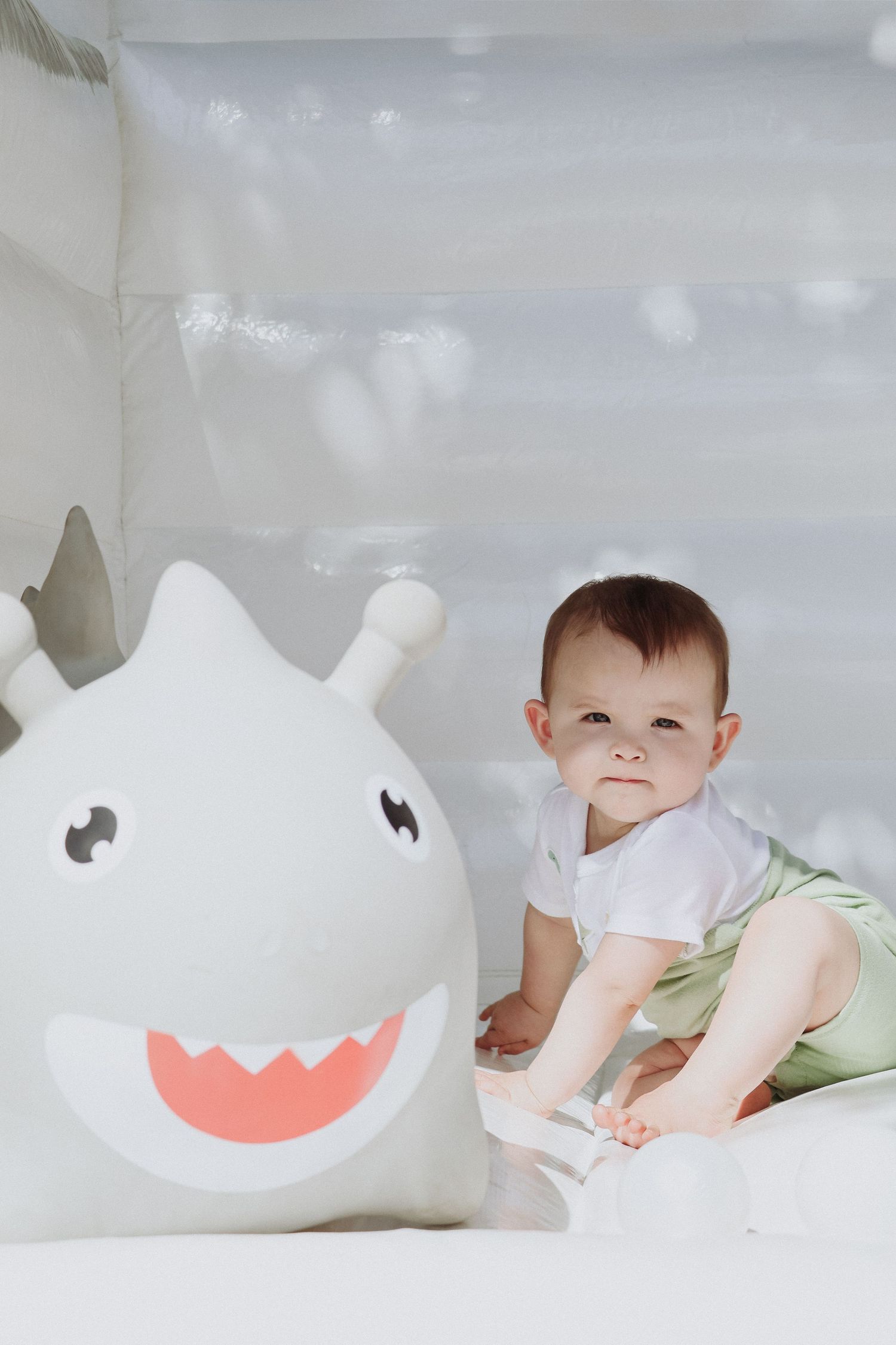 Baby interacting with white decorative plush character on light background.
