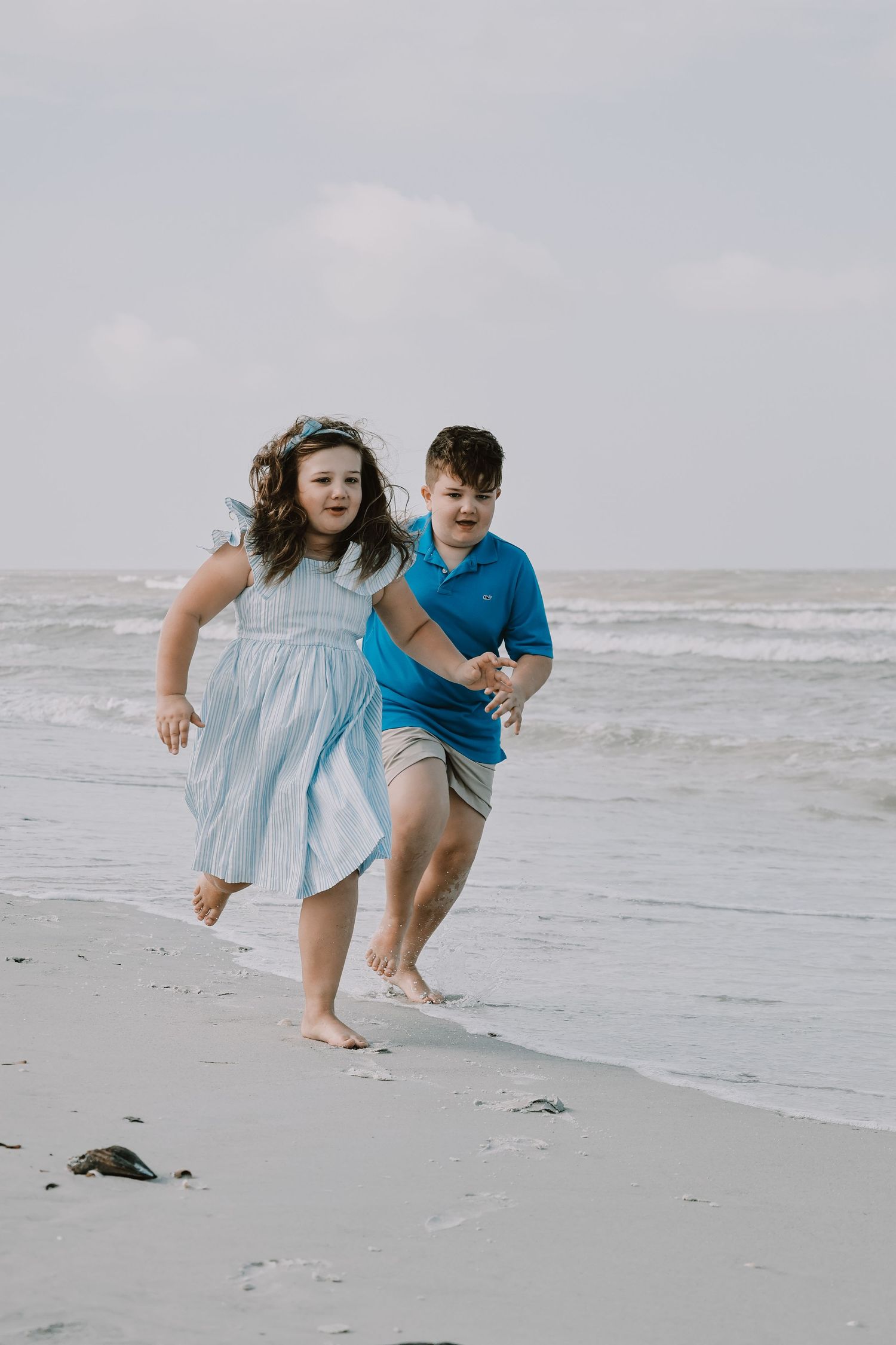 Two people running and playing along a cloudy beach shoreline.