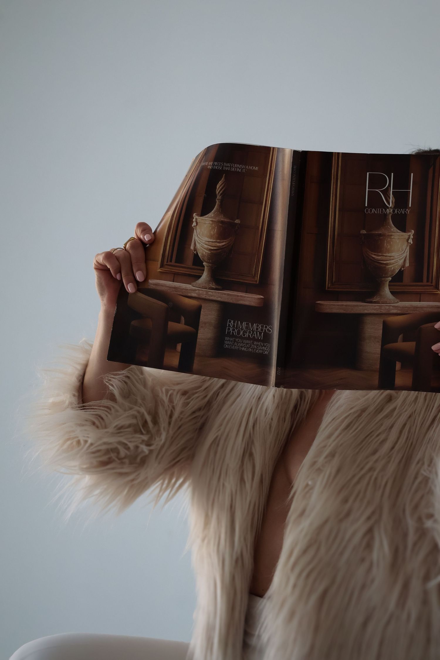 Close-up of hands holding luxury design book with furry jacket sleeve visible.