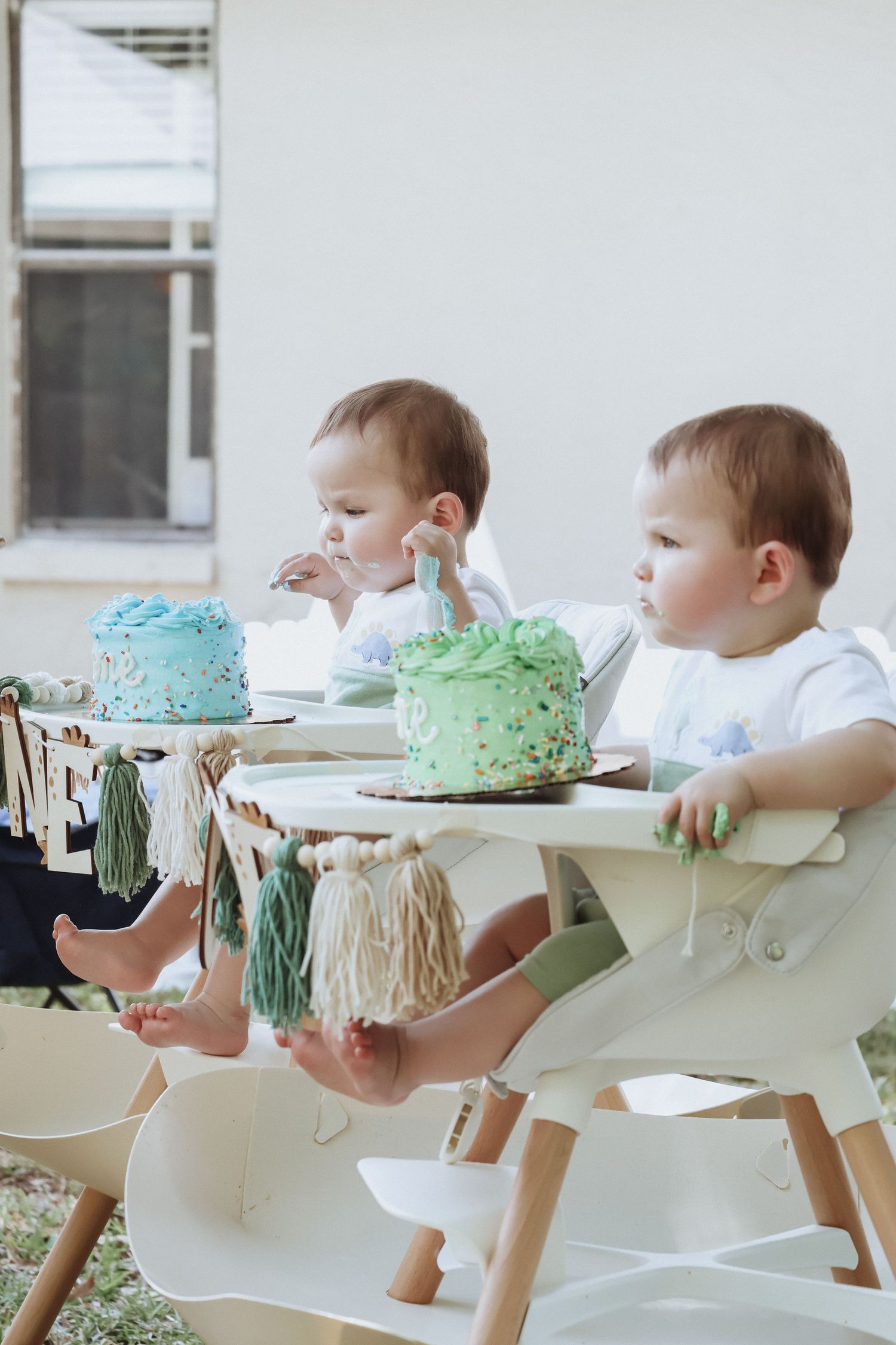 Two high chairs with blue and green smash cakes decorated with tassels.