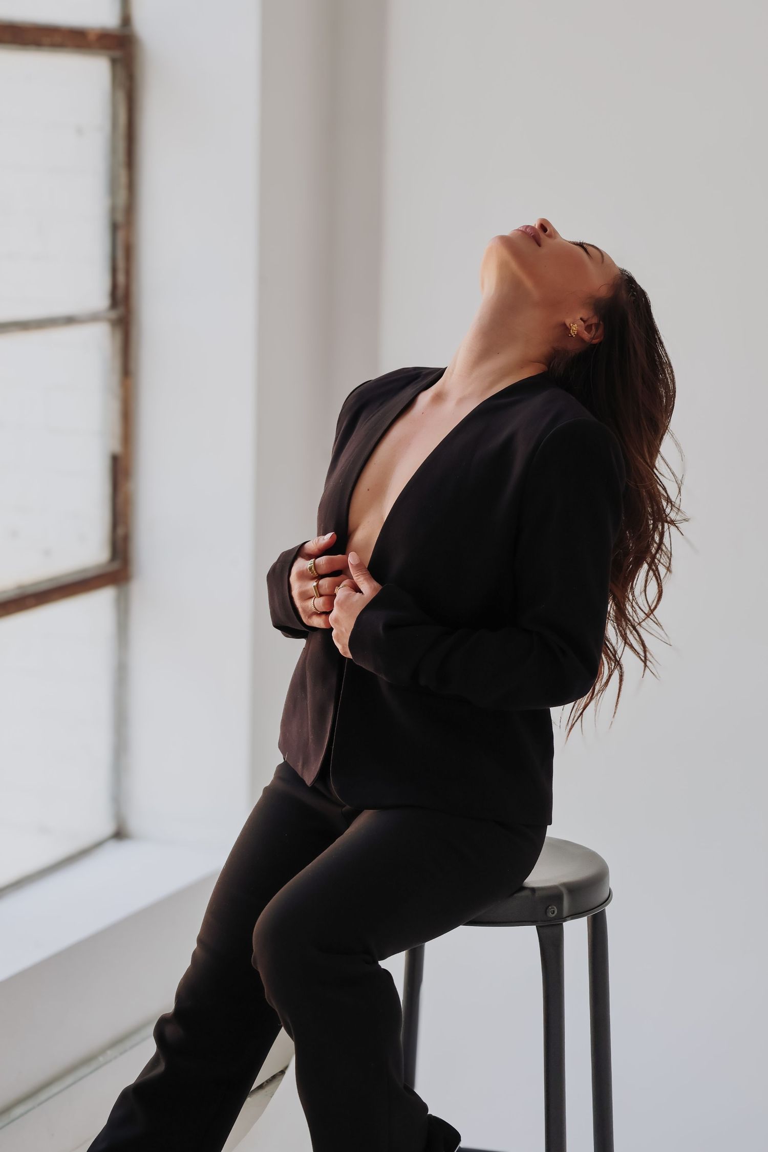 Dramatic fashion pose in black blazer against minimalist white studio setting.