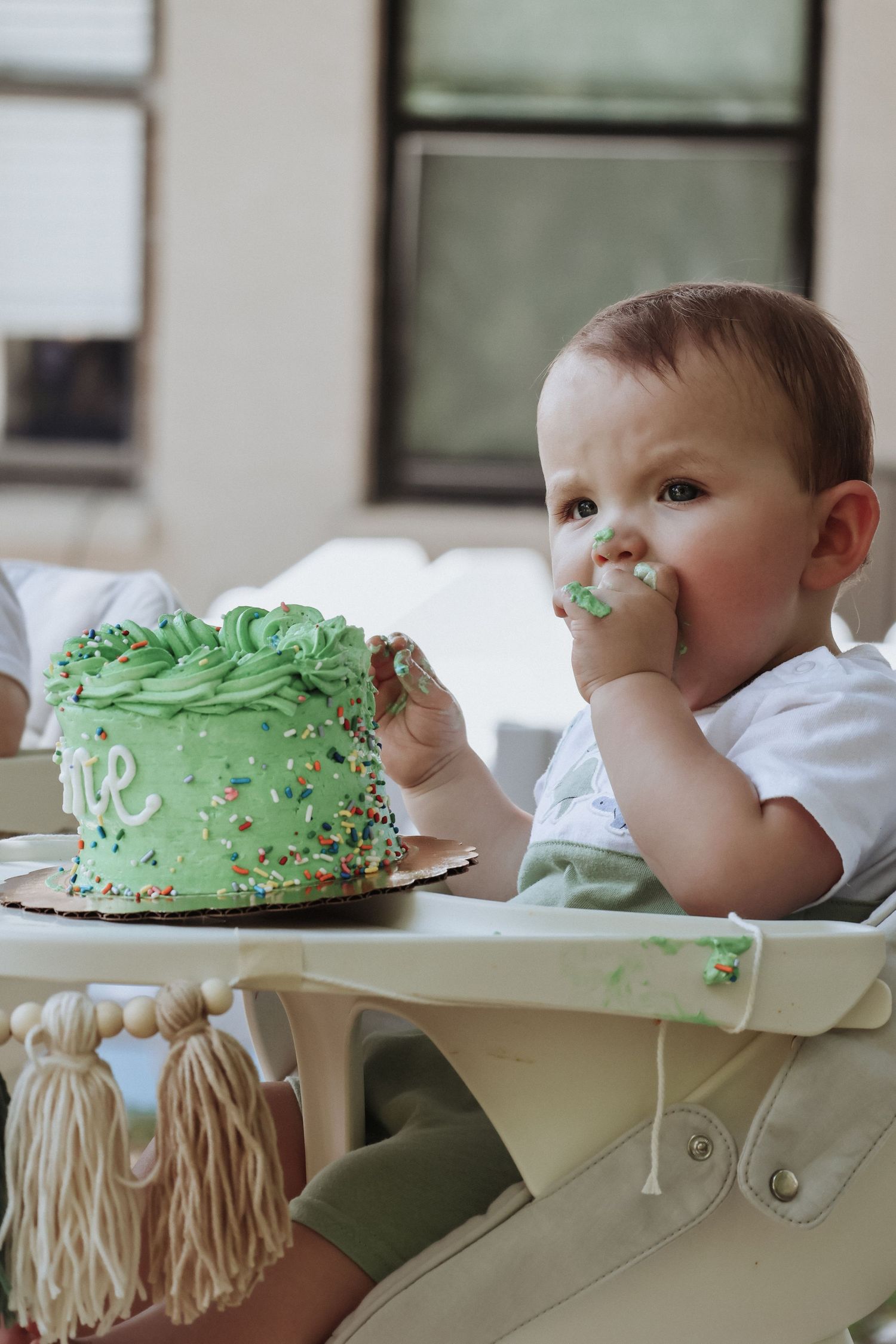 Green birthday cake being enjoyed by messy eater in high chair.