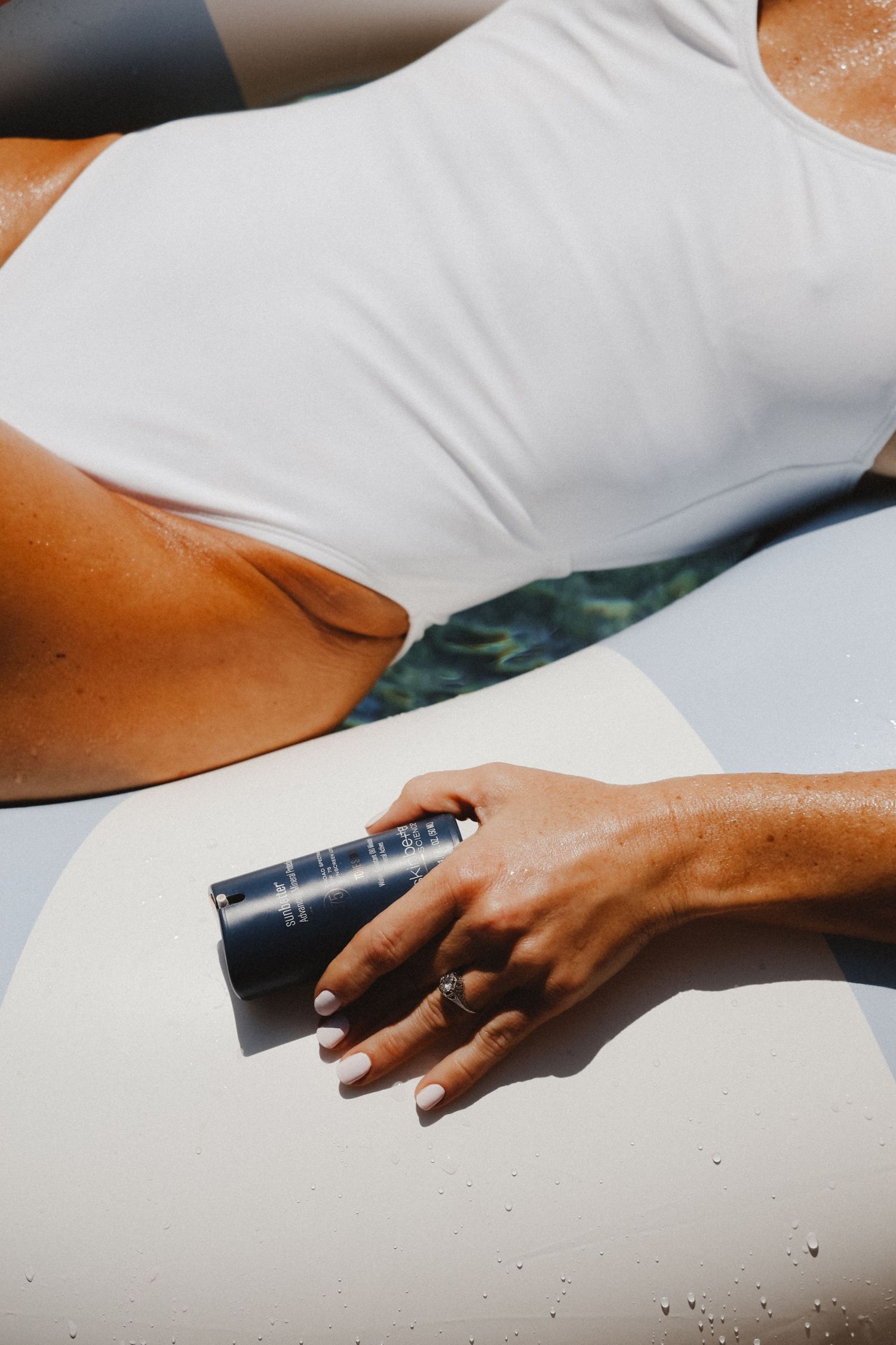 Hand holding sunscreen bottle against white swimsuit in bright sunlight.