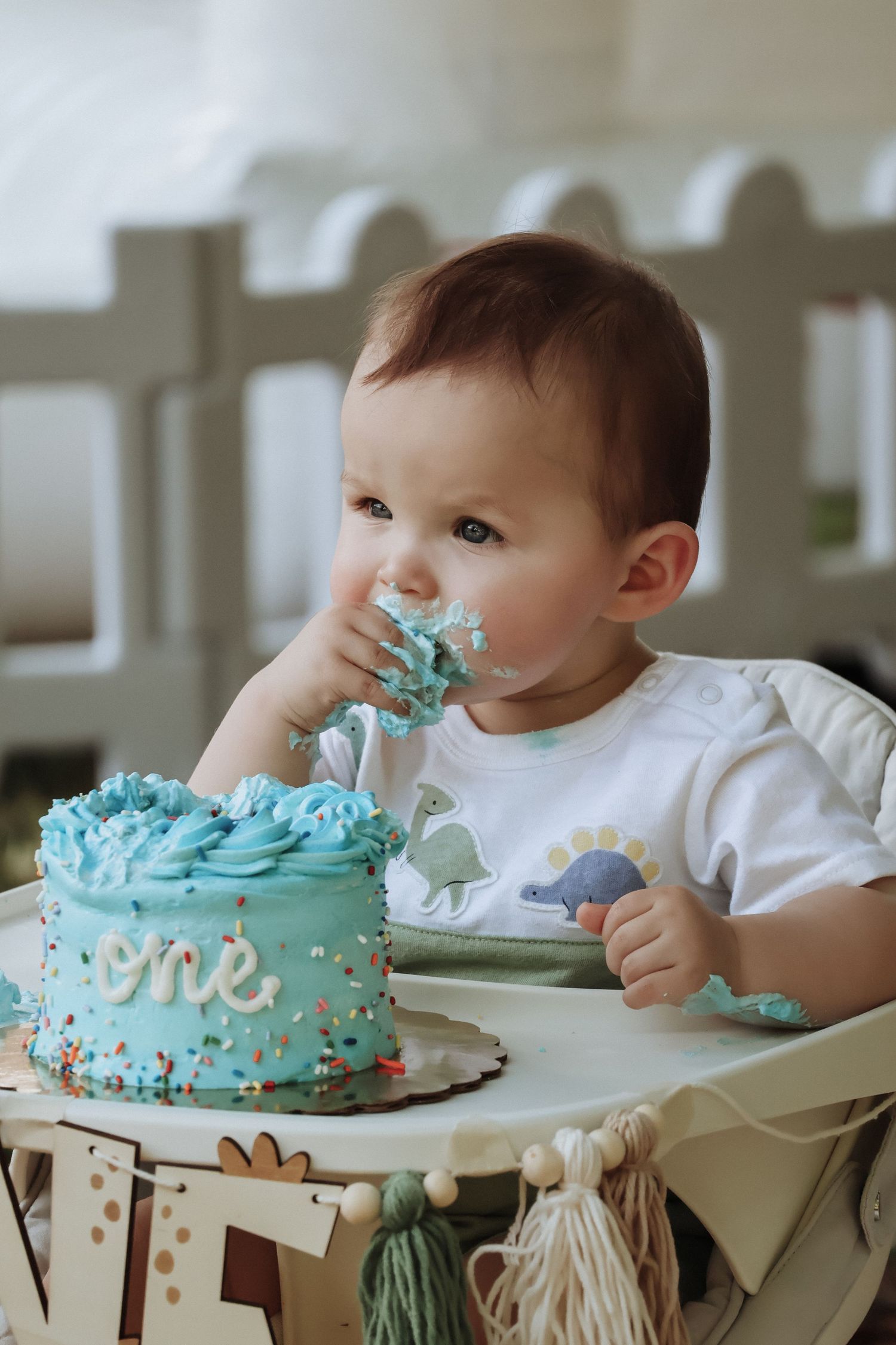 Baby in high chair eating blue birthday cake with messy frosted face.