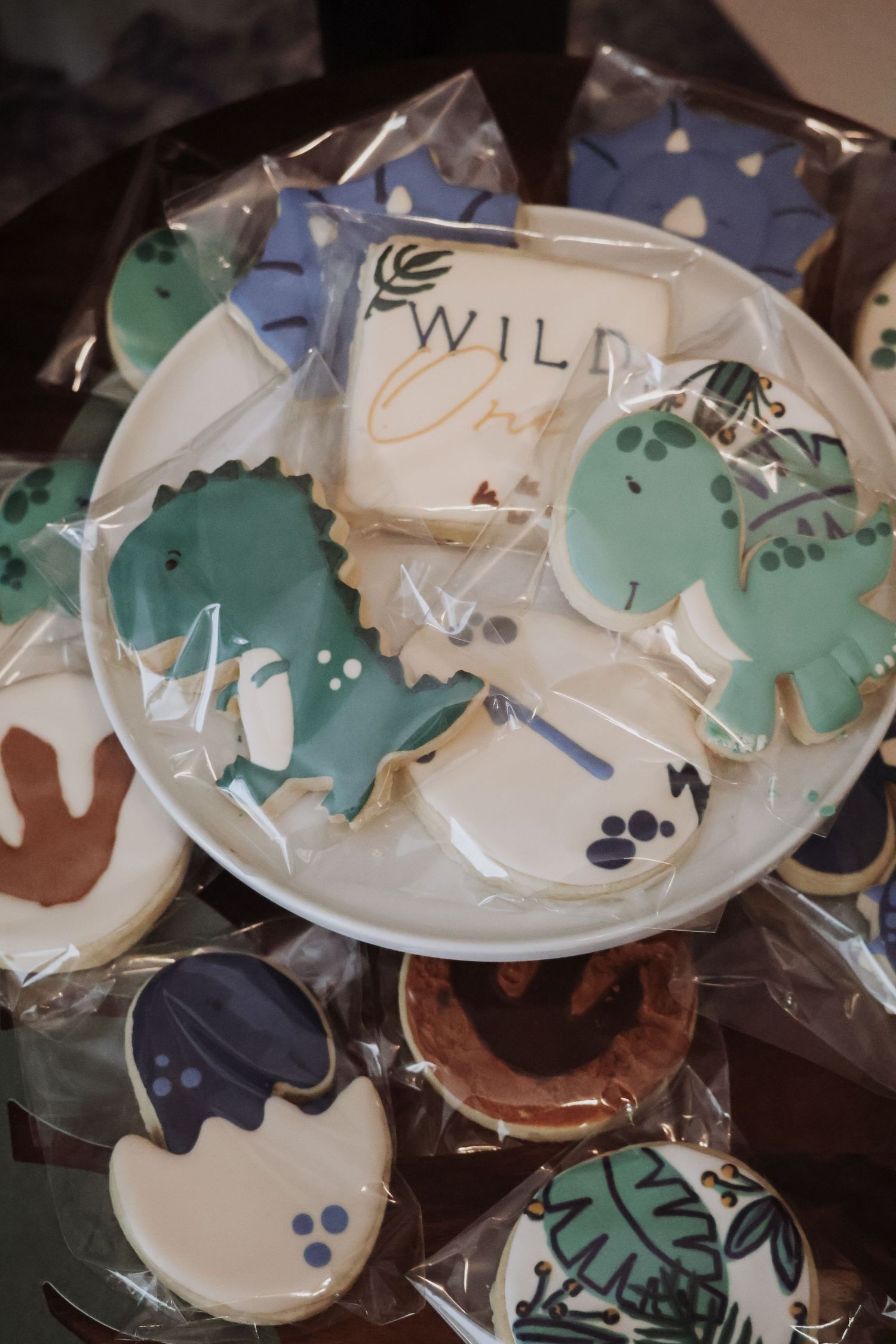 Decorative dinosaur-themed sugar cookies with blue and green icing displayed on a white plate.