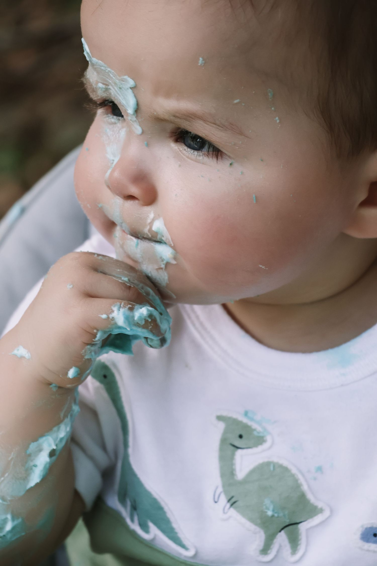 Close-up of messy cake frosting on face while wearing dinosaur shirt.
