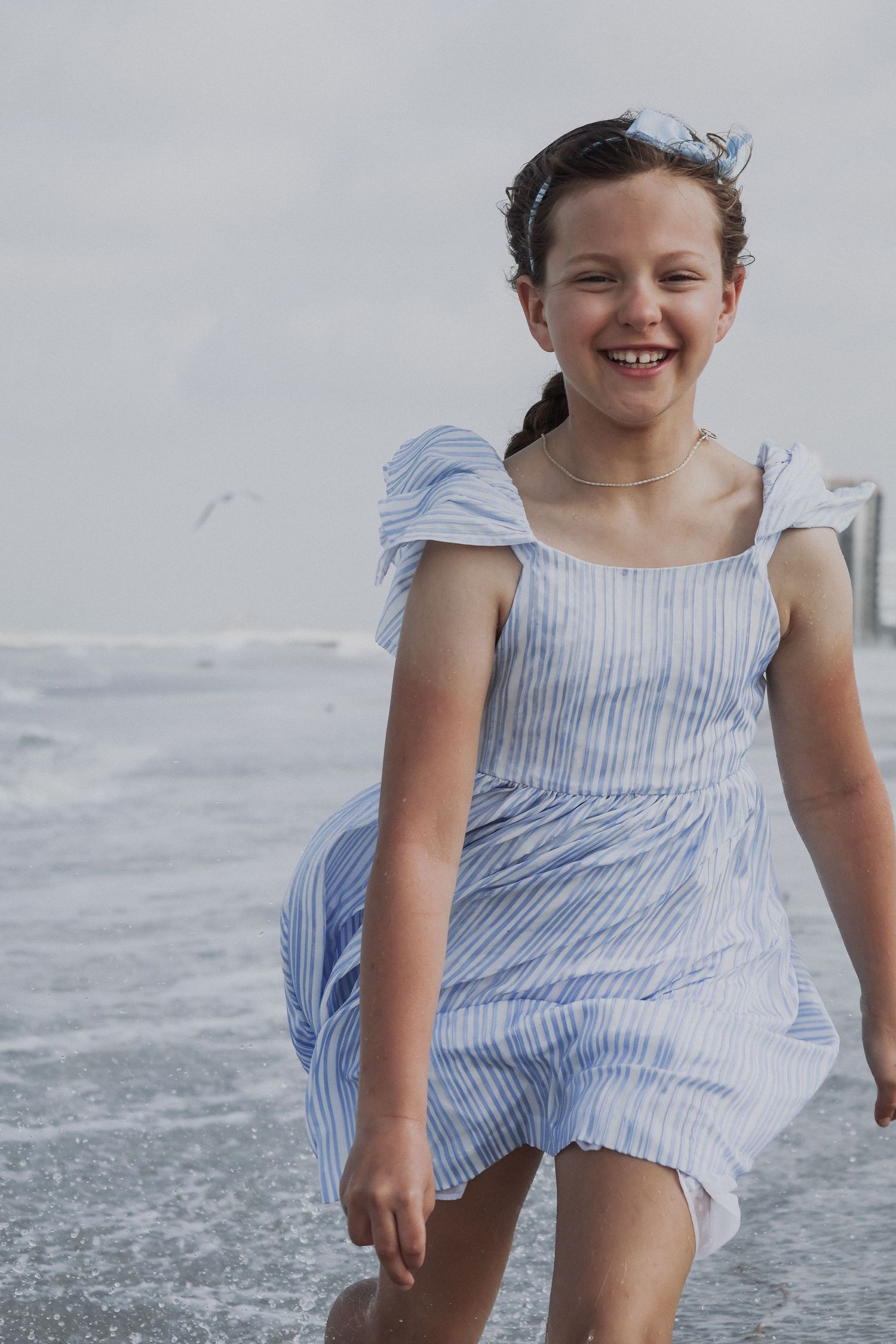 Person in blue striped dress smiling while enjoying a breezy day at the beach.