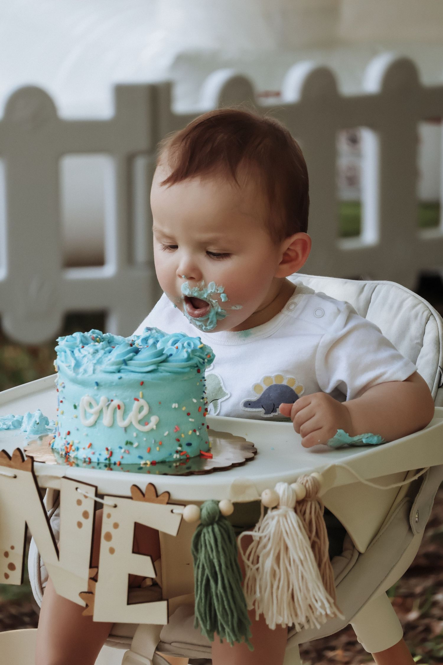 Baby in high chair enjoying first birthday cake with blue frosting.