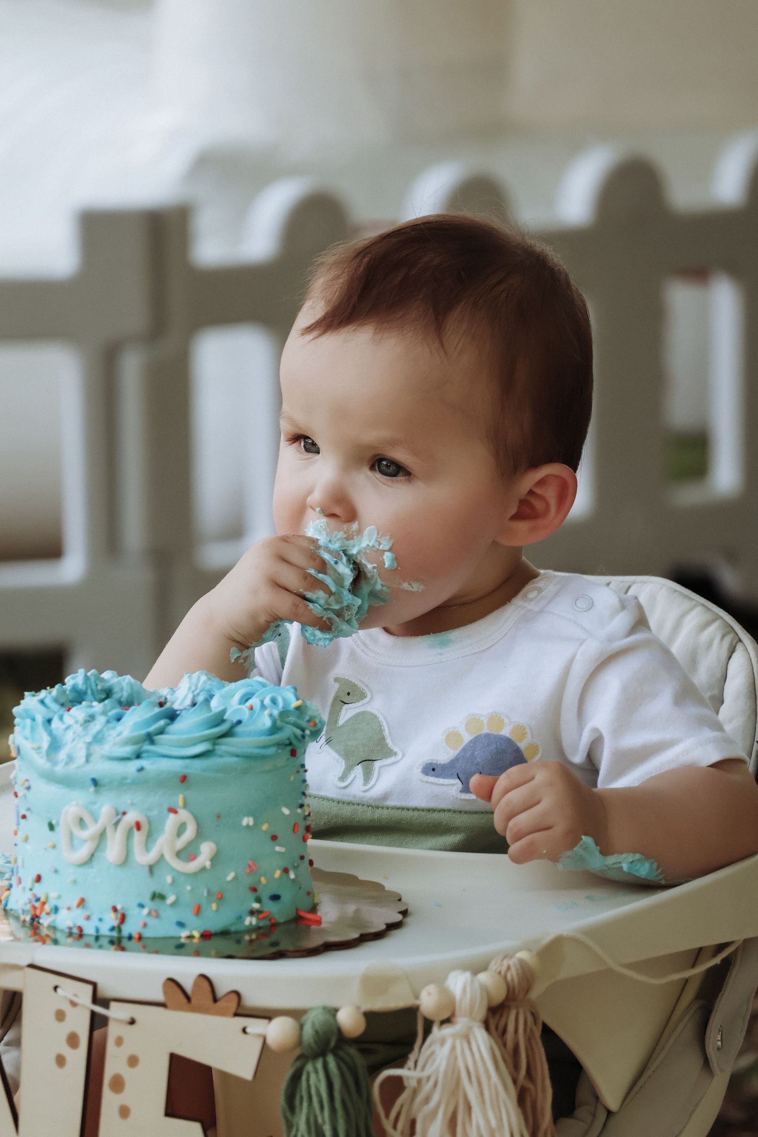 Small child in high chair eagerly grabs blue frosted birthday cake.