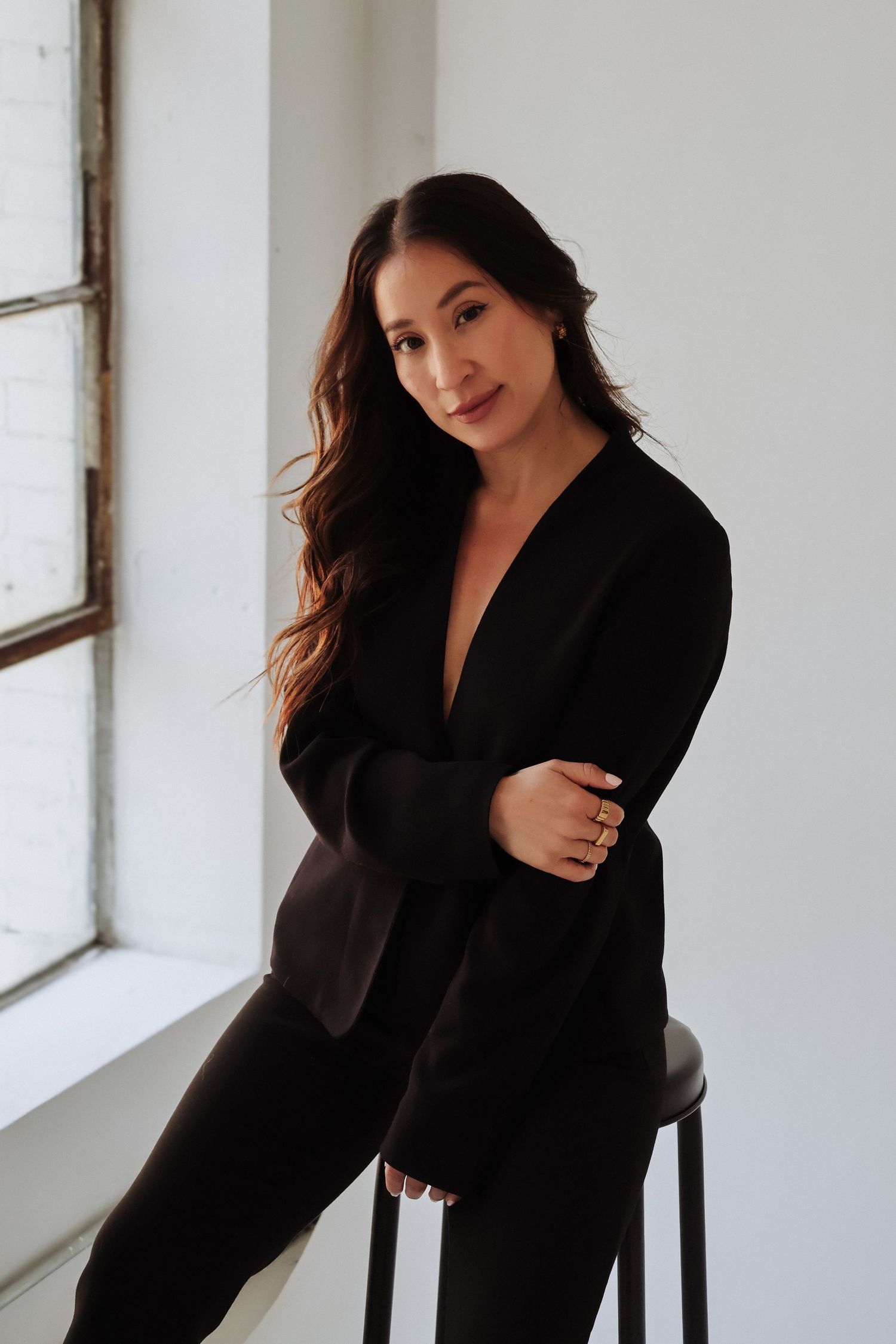 Professional fashion model poses in black blazer against white studio wall.