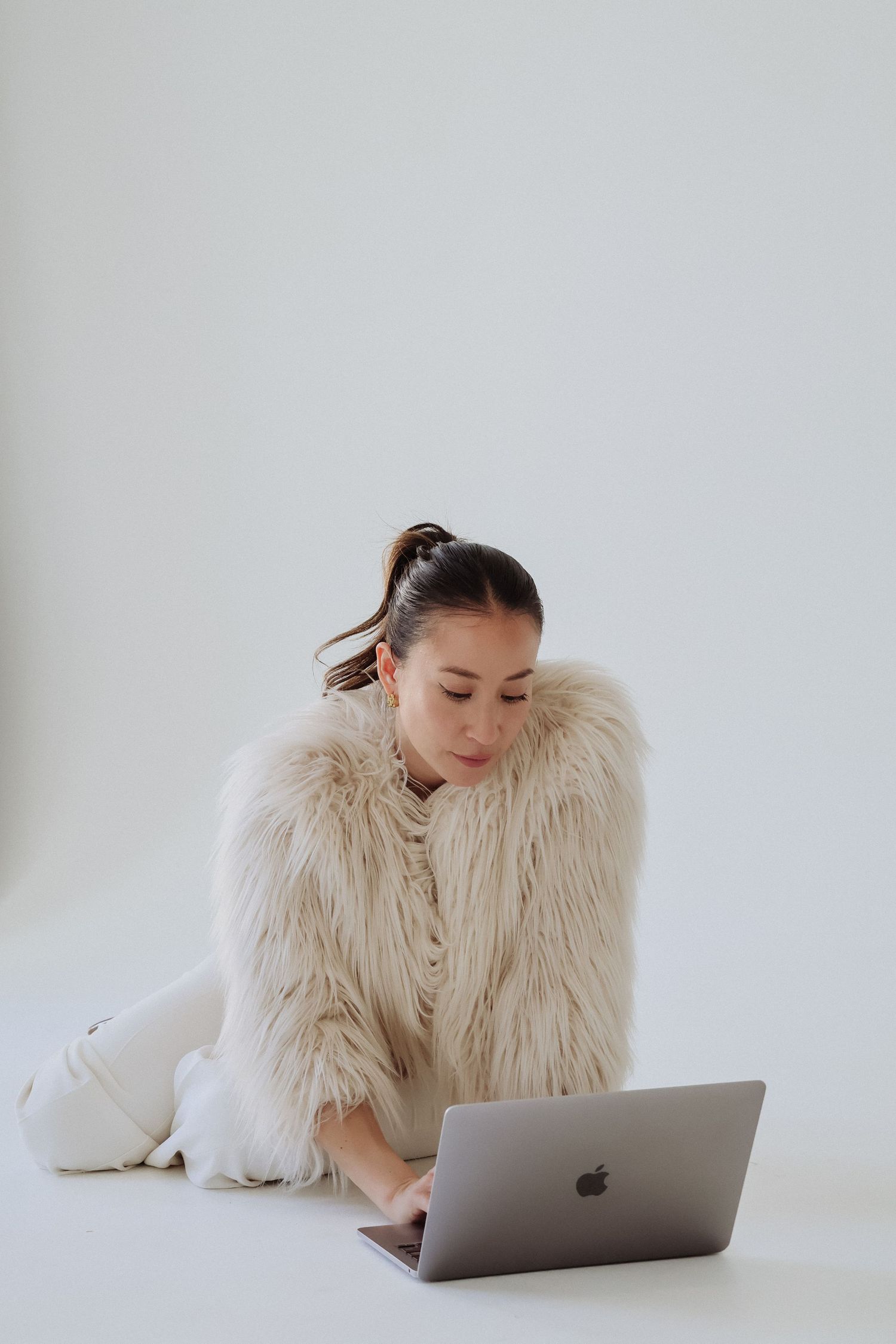Person in fluffy white coat working on MacBook laptop against white background.
