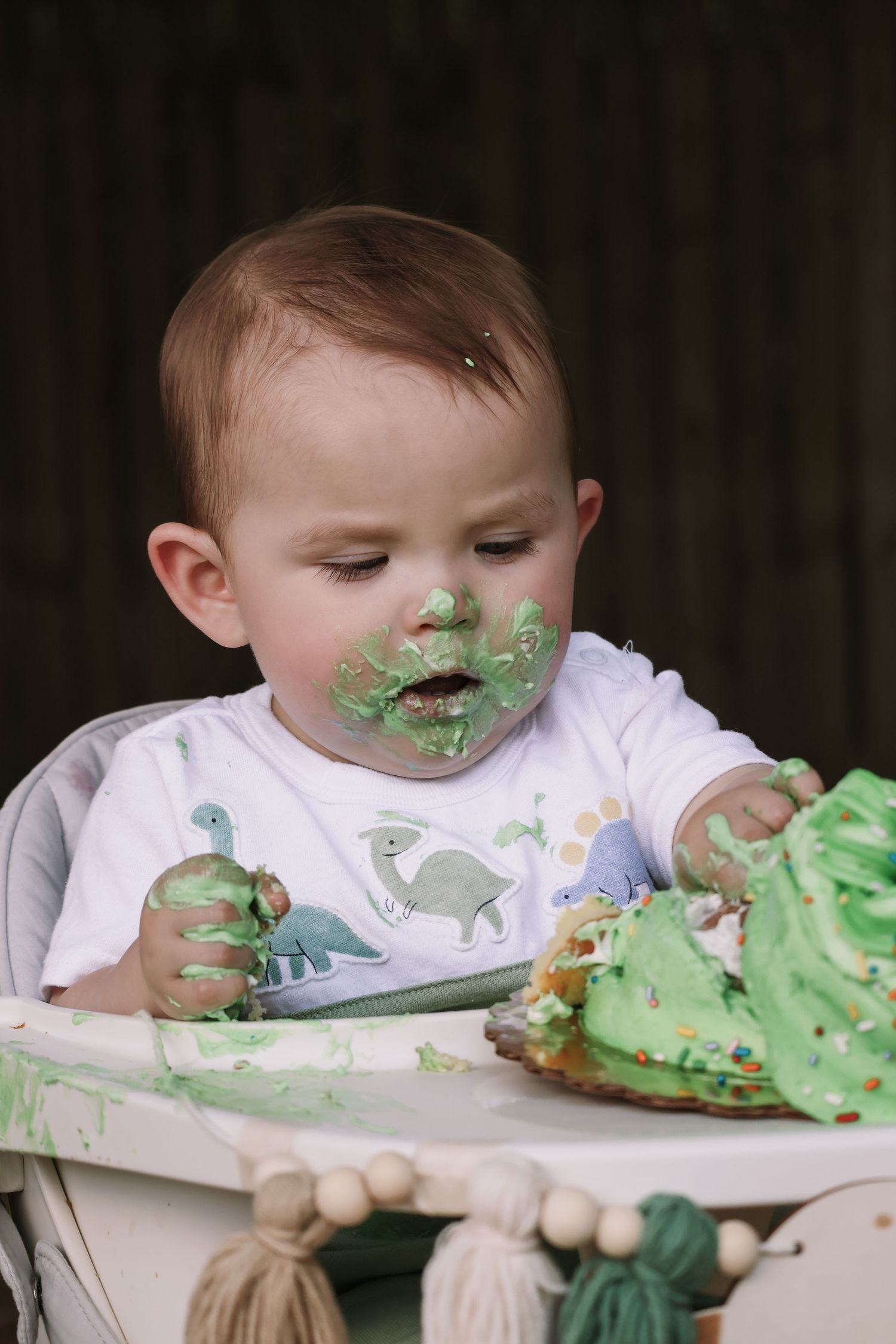 Green frosting covers face as small child enjoys birthday smash cake.