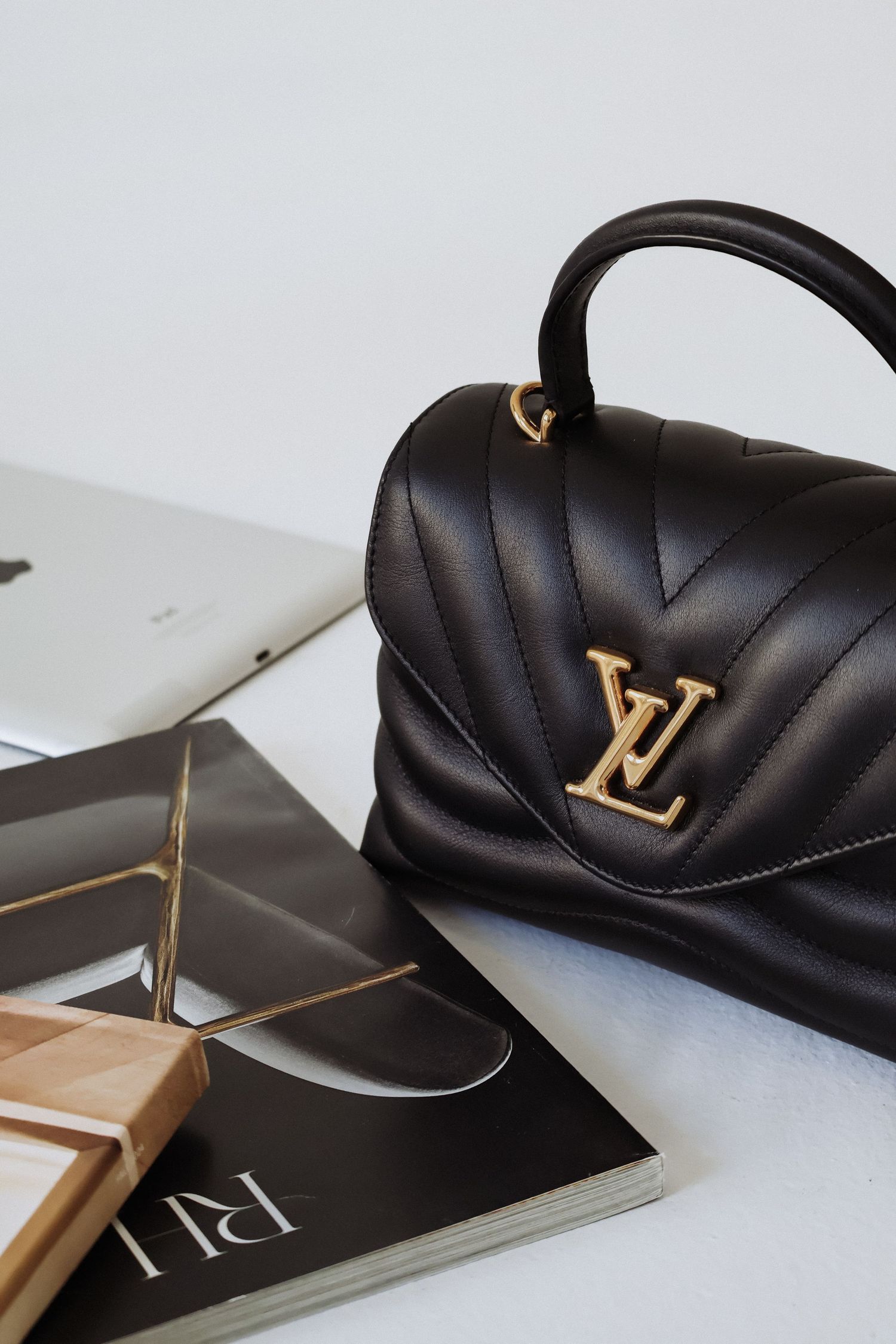 Black Louis Vuitton handbag with gold hardware displayed with magazines and MacBook.