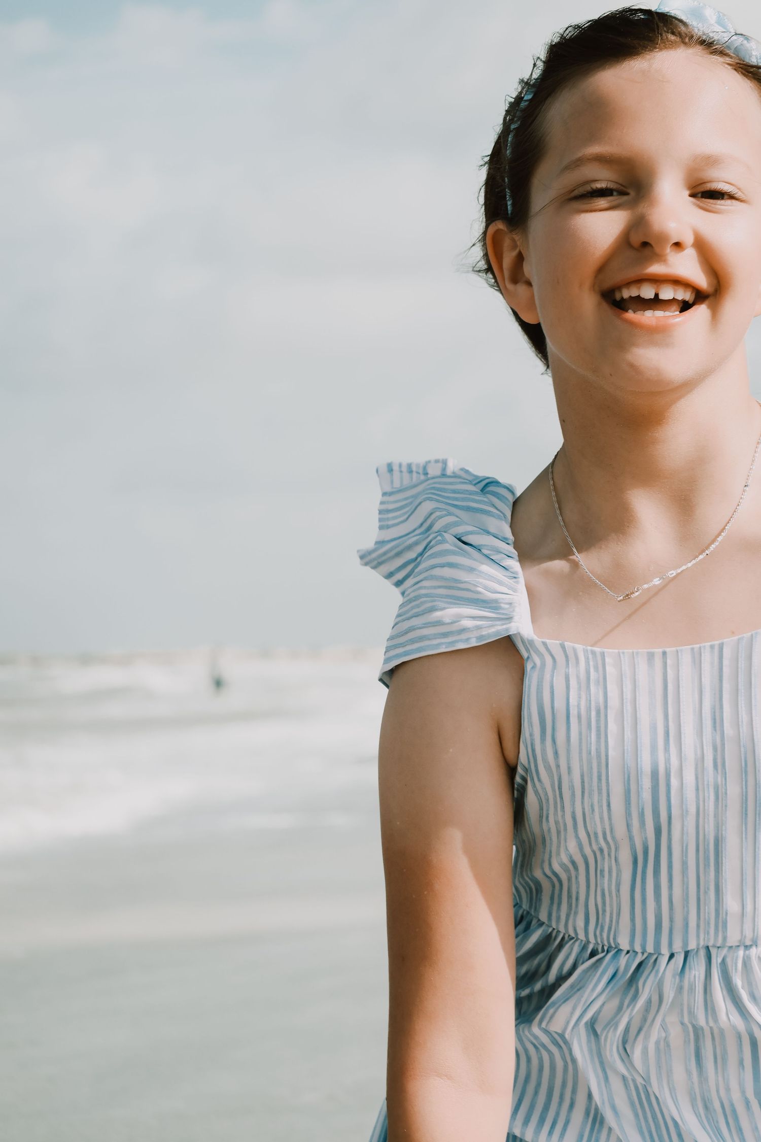 Close up portrait of person wearing a blue striped dress at the beach.
