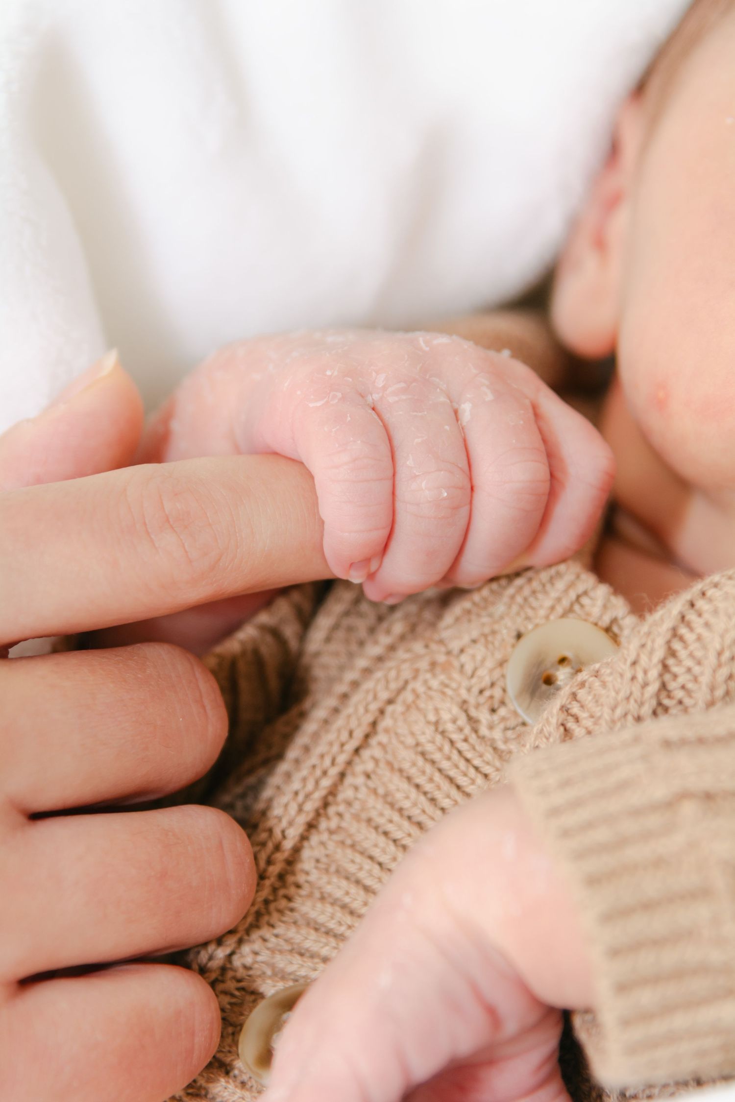 Multiple shots of tiny baby hands holding adult fingers against beige knitted fabric.