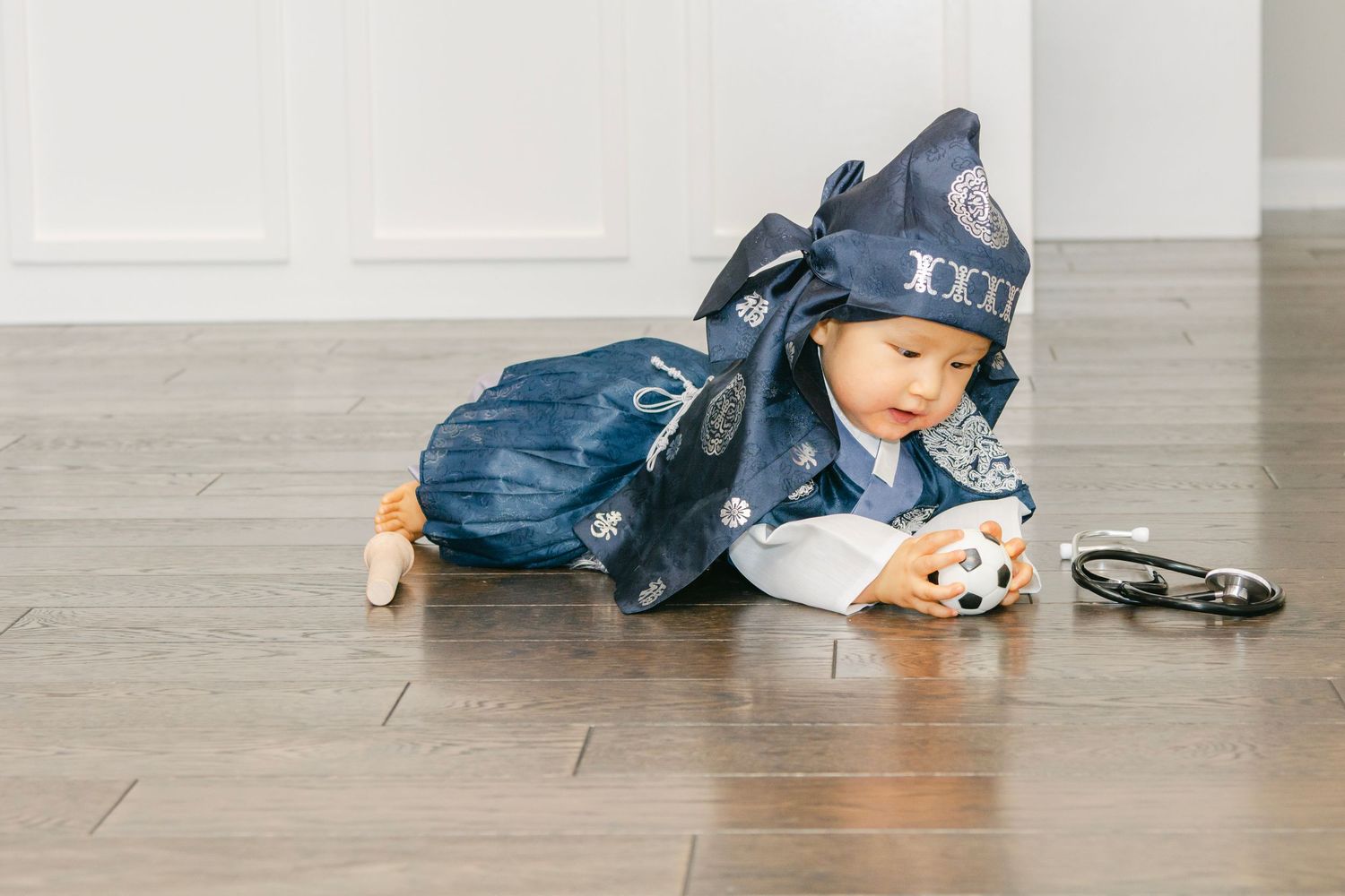 Child in blue clothing crawling on hardwood floor near party decorations.
