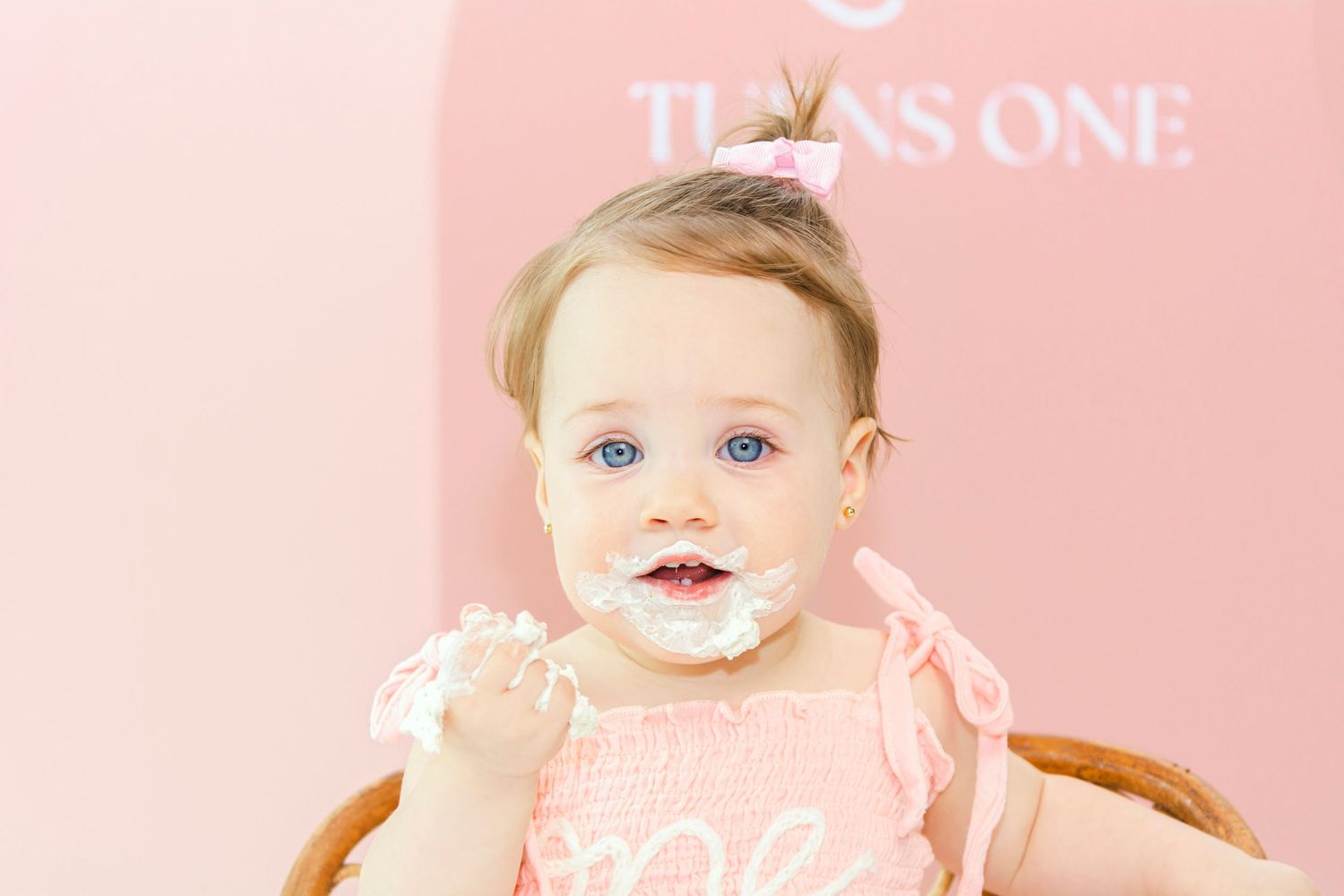 Baby's first birthday cake smash photography setup with pink pastel decor and wooden chair.