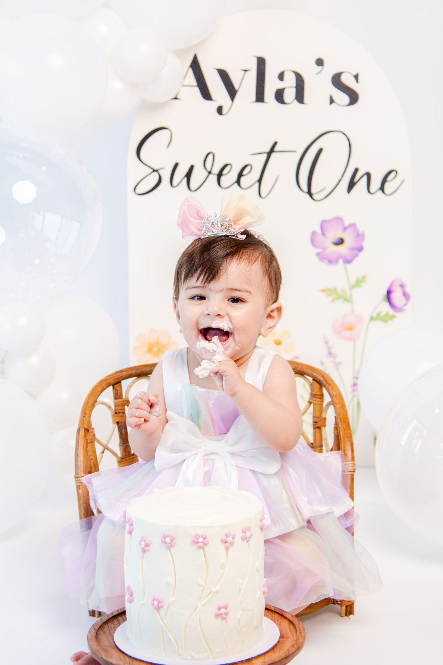 Baby girl in pink dress celebrating first birthday with elegant white cake.