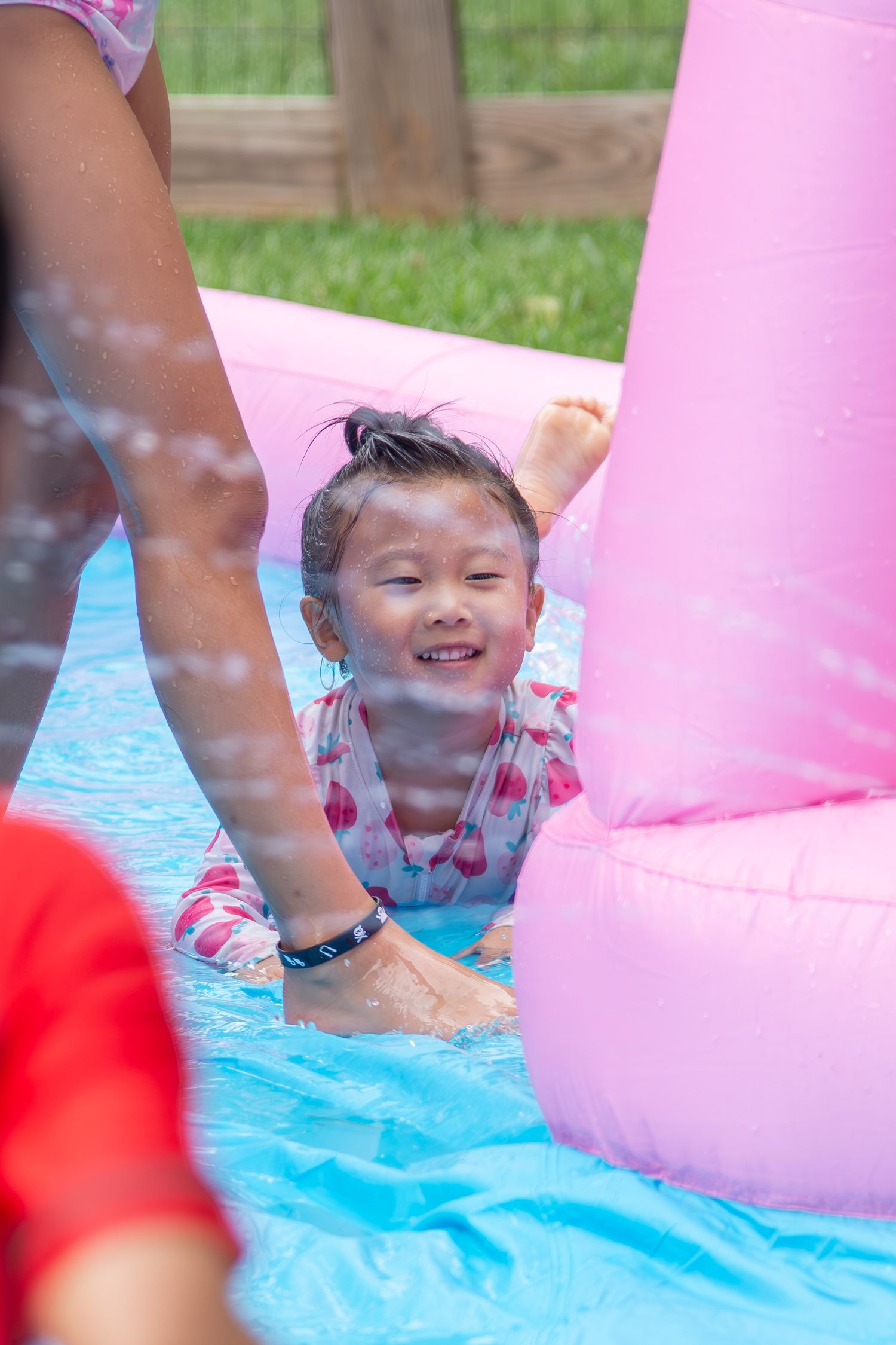 Child playing in a backyard water activity with pink inflatable toys and blue mat on a sunny day.