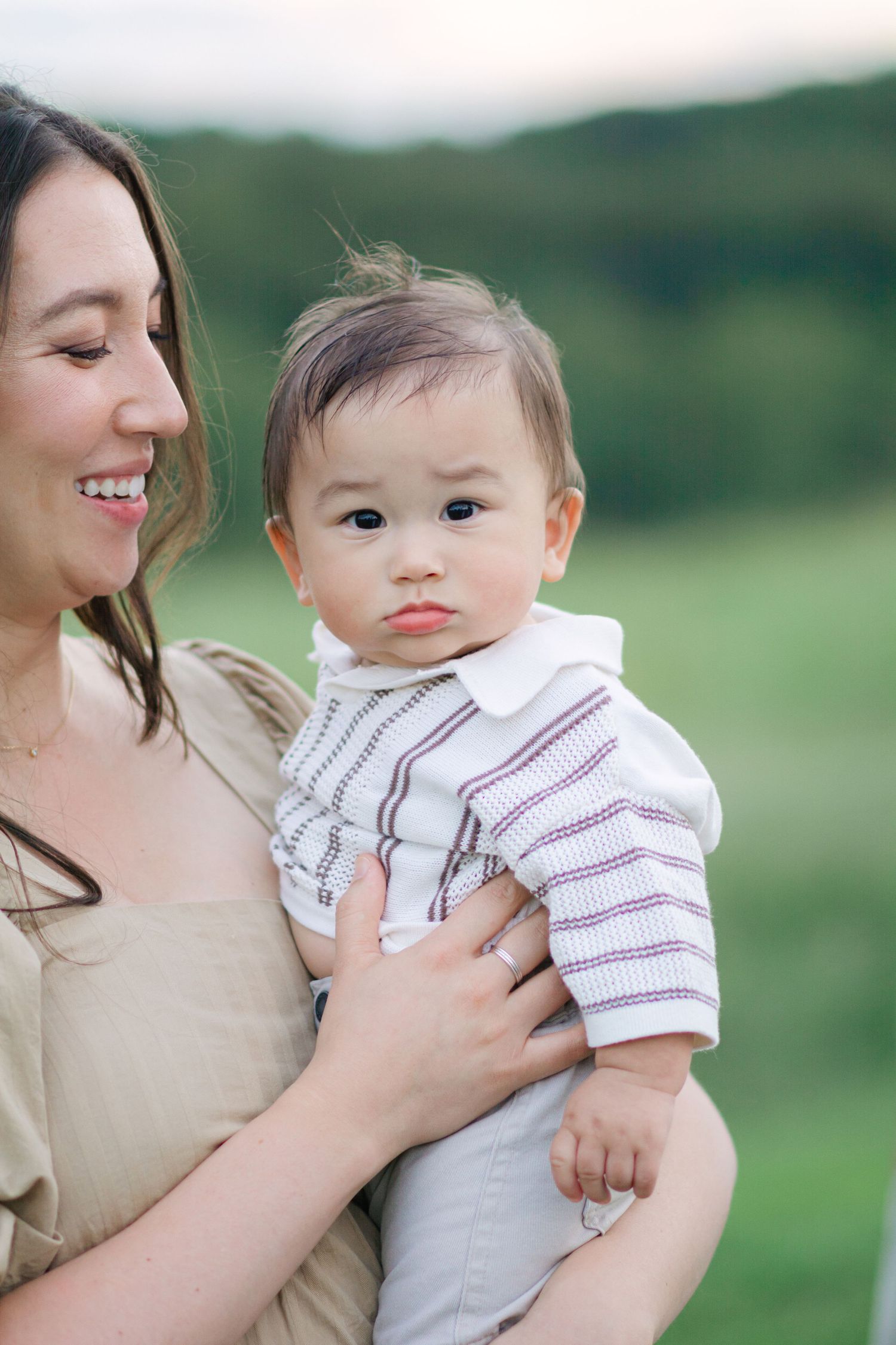 Mother holding infant in striped outfit while sharing tender moments outdoors.
