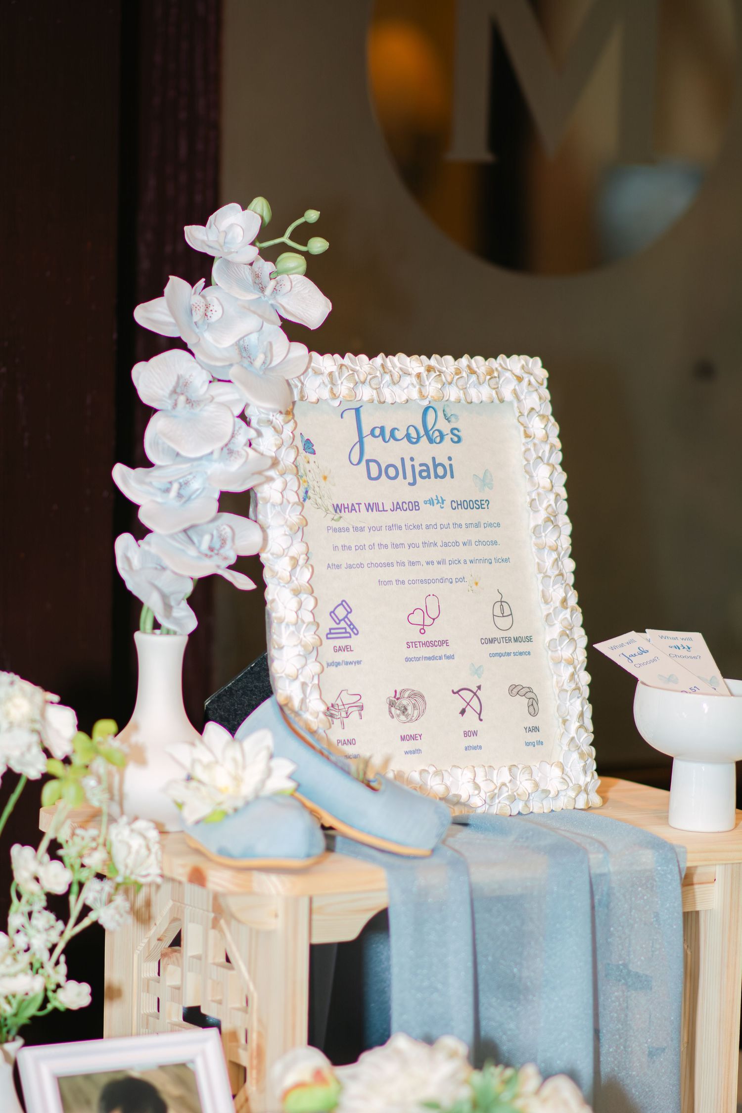 Baby-themed party decor featuring white frames, blue books, and delicate floral arrangements.