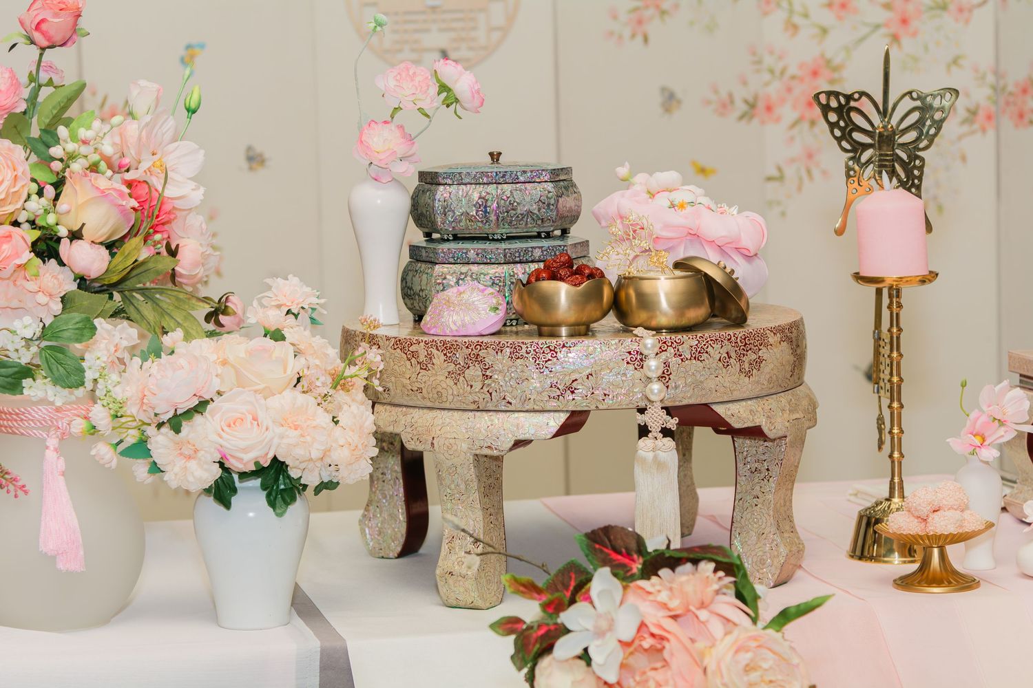 Vintage-style decor table with pink flowers, metallic accents, and butterfly ornaments.