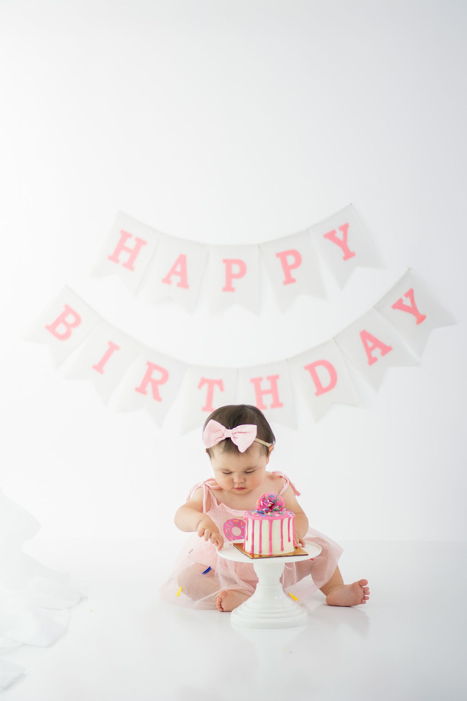 Baby's first birthday cake smash session with pink birthday banner and white decorations.