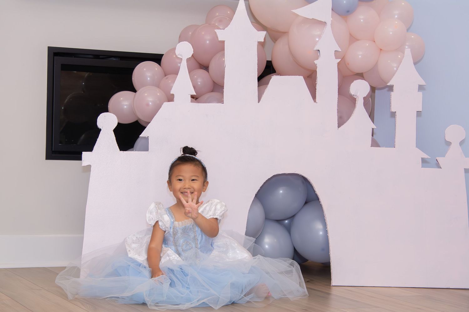 A baby's first birthday photo session with blue and pink balloons, white castle backdrop, and tulle dress.