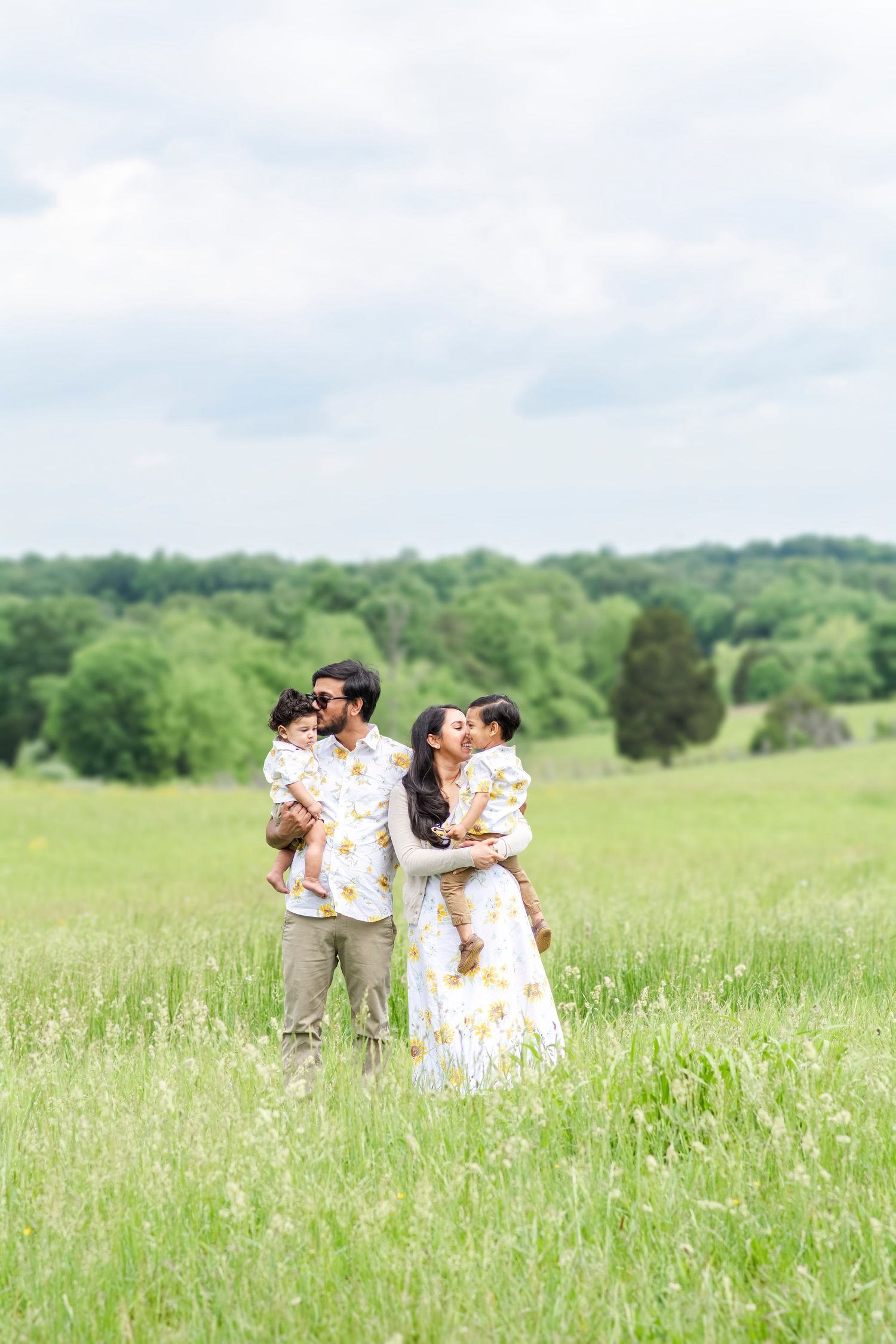Family portrait in flowering meadow wearing coordinated outfits on bright spring day.