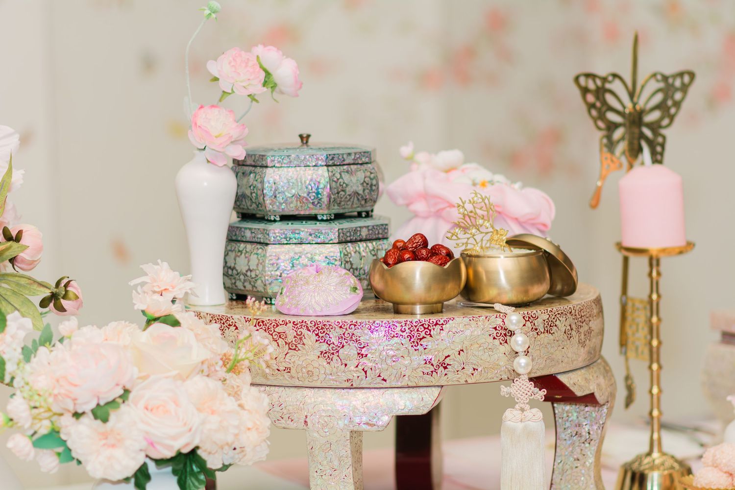 Decorative table setting with antique boxes, gold vessels, and pink floral arrangements.