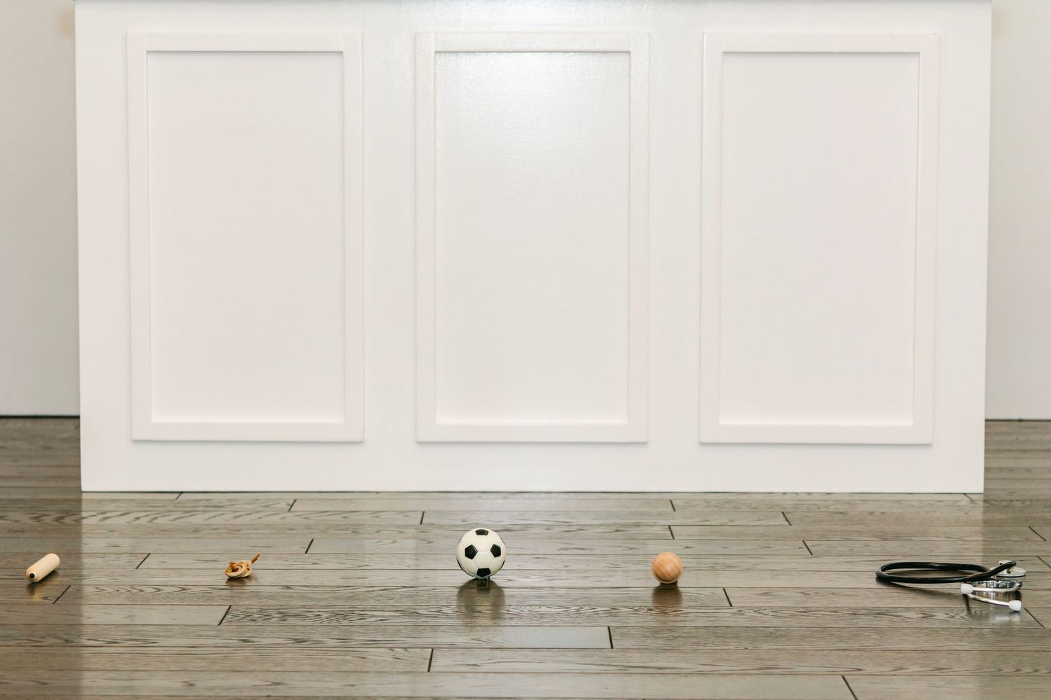 Clean white paneled wall with scattered toys on hardwood floor.